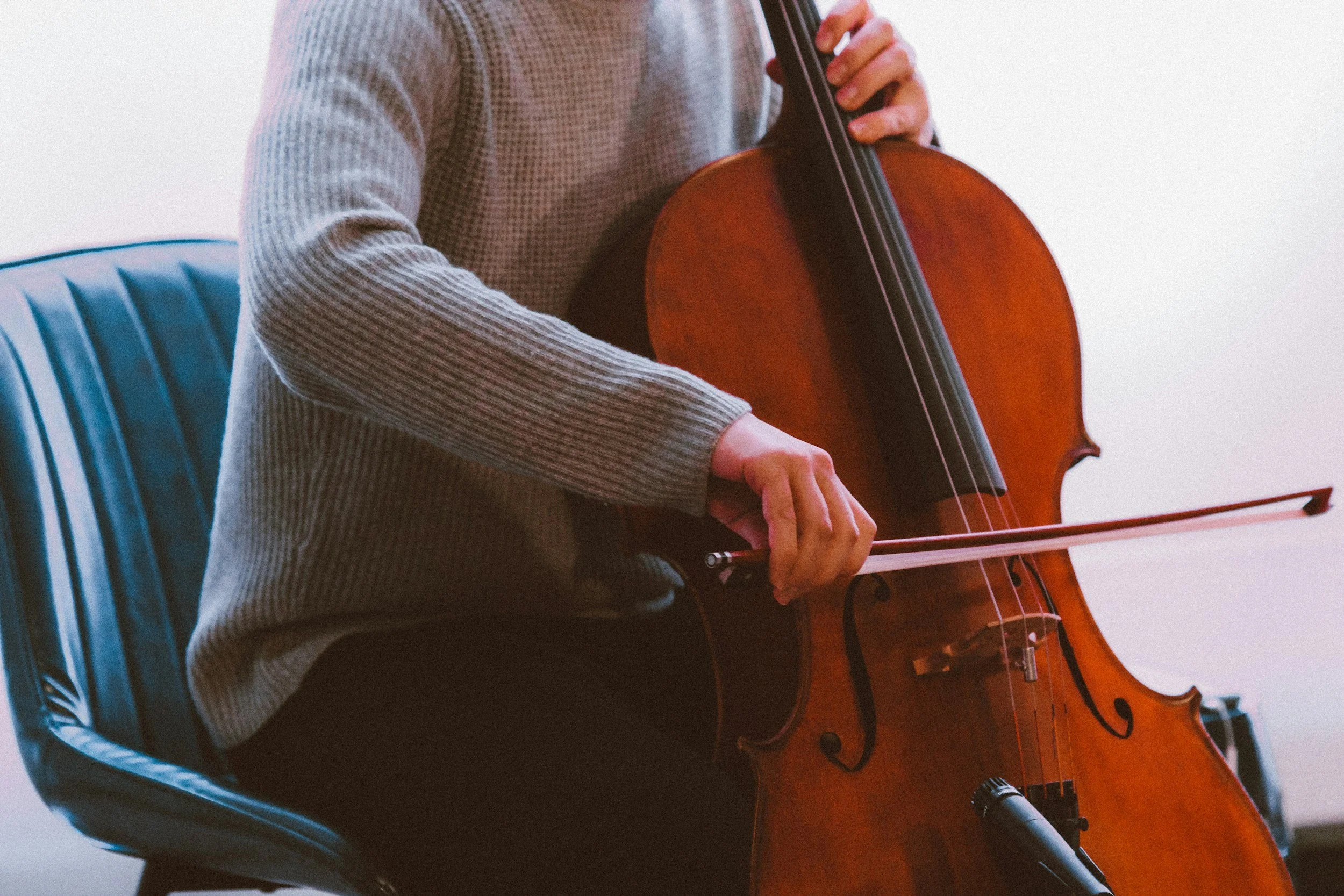 A person playing the cello with a bow sat at home.