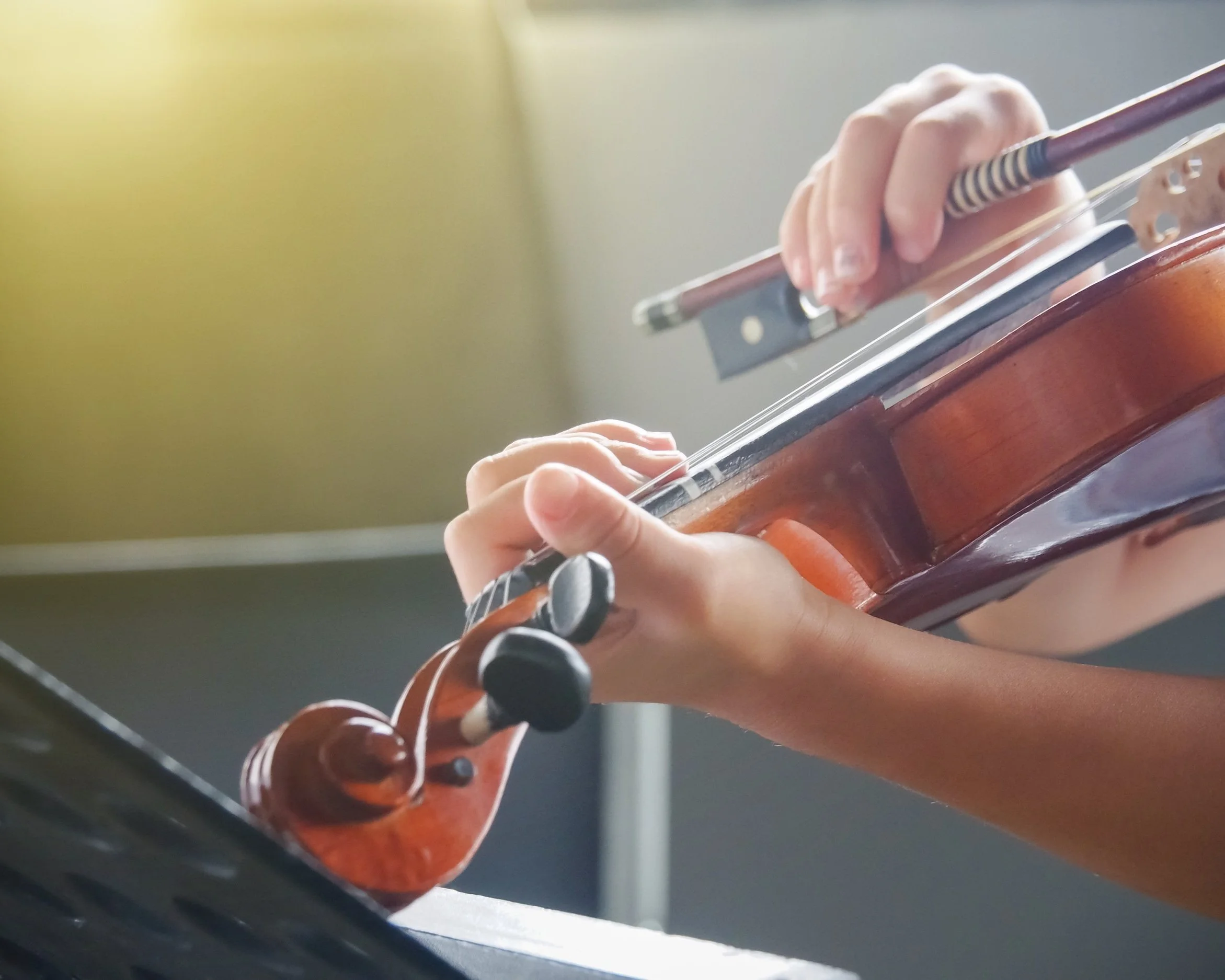 Close-up of child playing the violin and reading sheet music during their lesson.