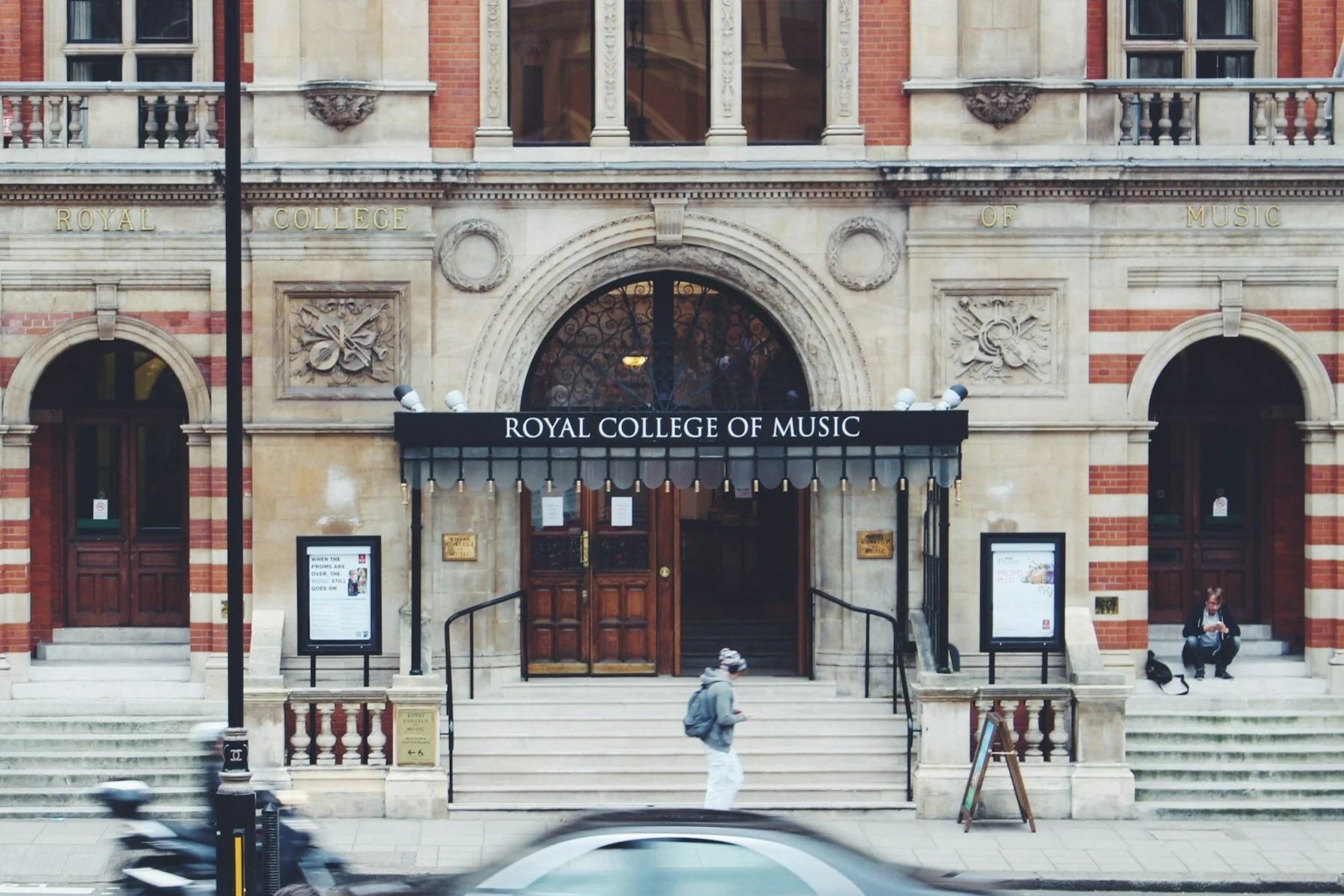 Entrance to the Royal College of Music with a student wearing headphones walking outside.