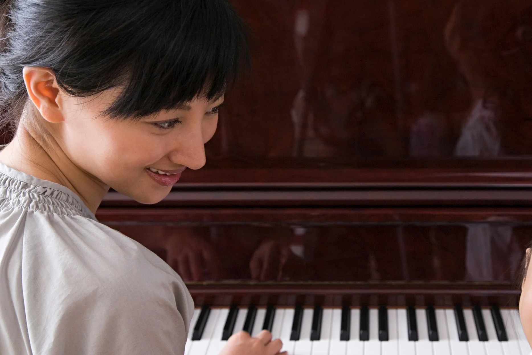 A woman with black hair smiling and looking down at a piano keyboard.