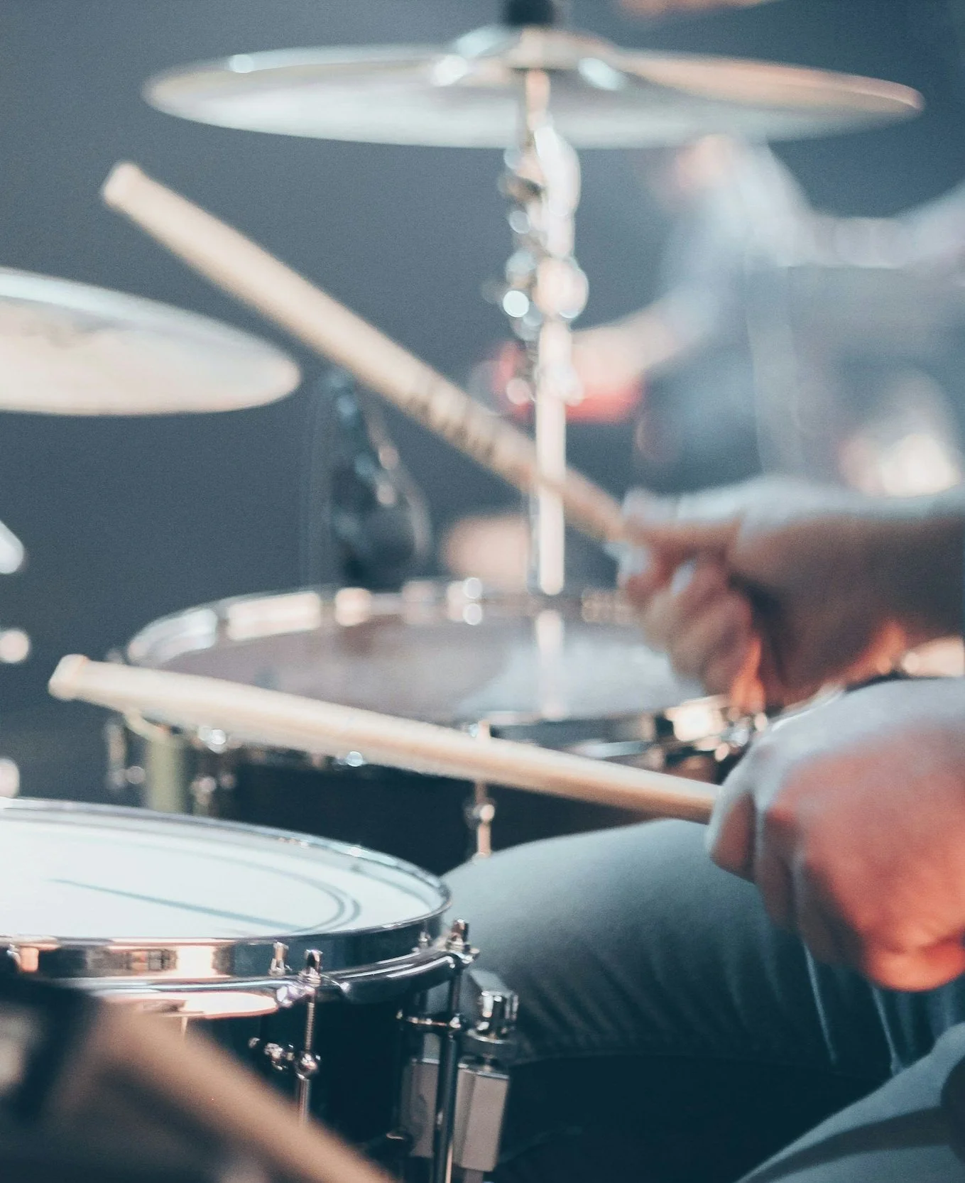 Close-up of someone playing a drum kit with drum sticks at home.