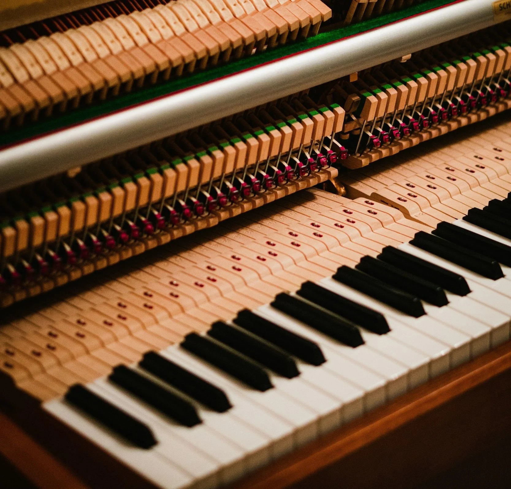 Close-up of the internal mechanics and keyboard of a piano, showing strings, hammers, and black and white keys.