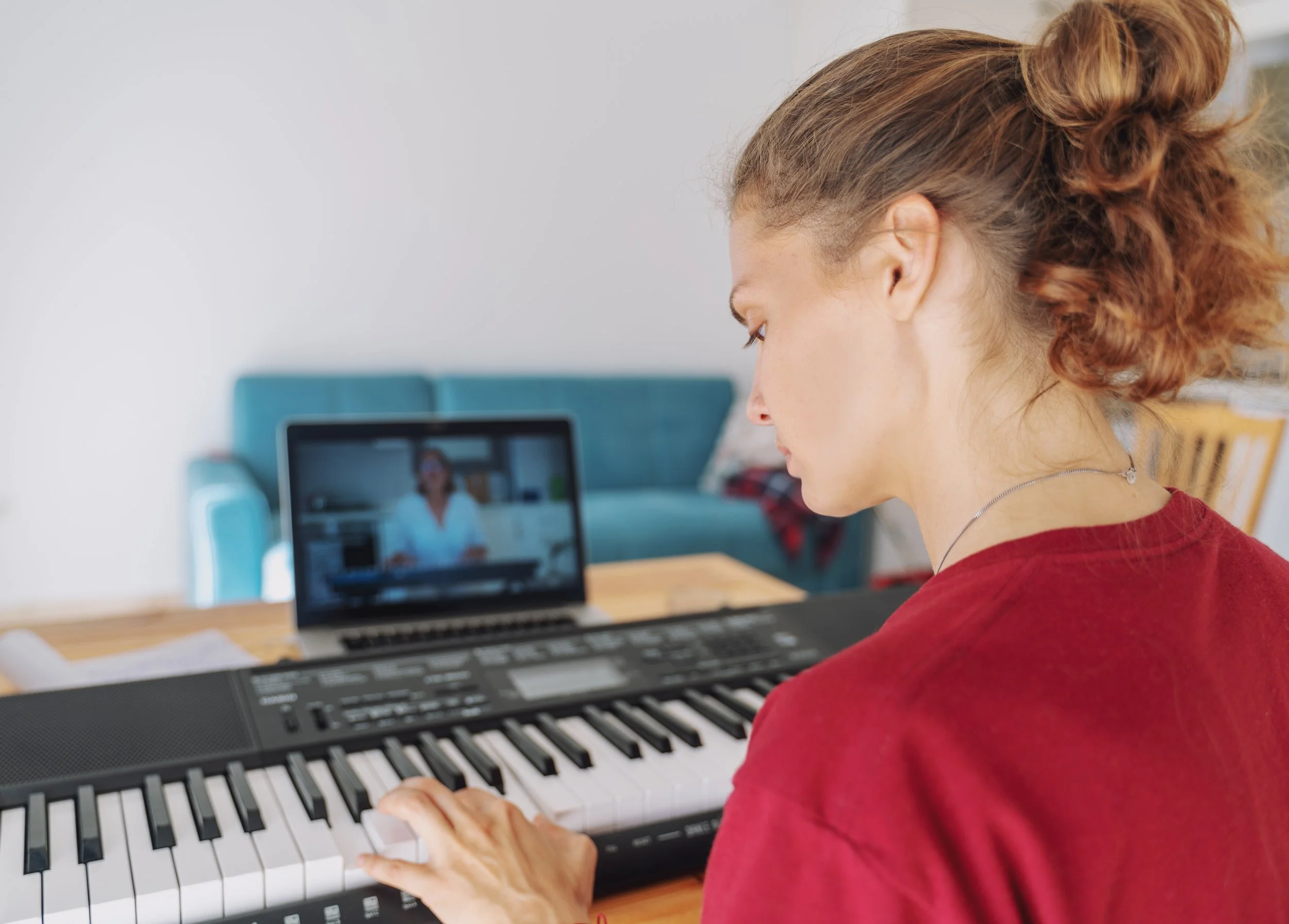 A woman having an online piano lessons with the teacher on a laptop screen.