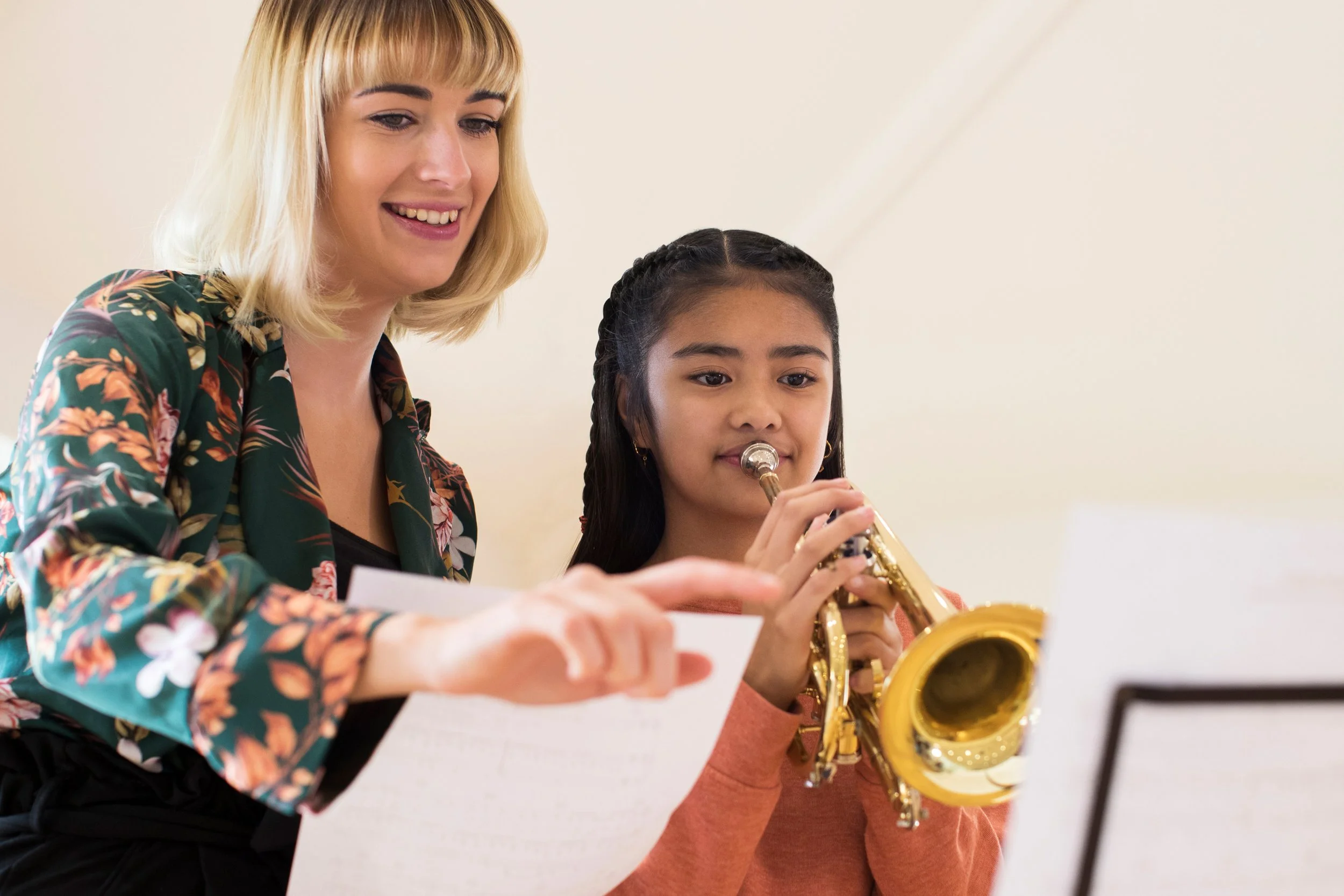 A young girl playing the trumpet with a teacher smiling in London.