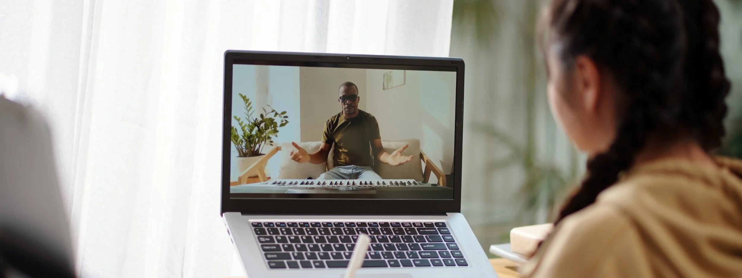 A piano teacher giving an online piano lesson whilst the student makes notes.