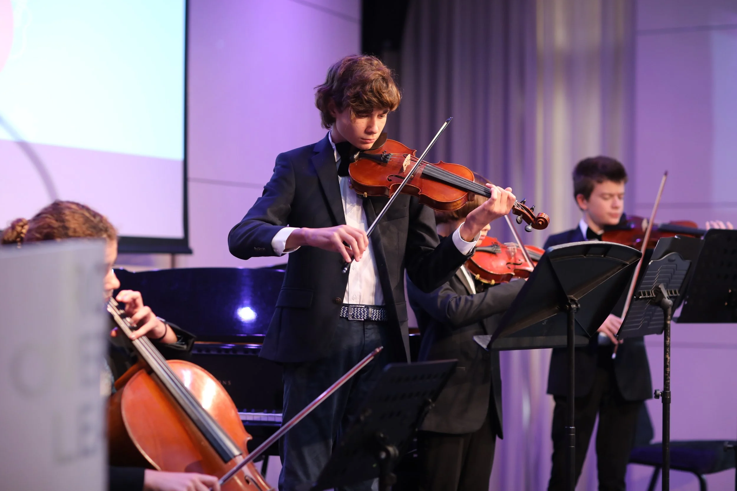 A boy playing the violin in a strings concert.
