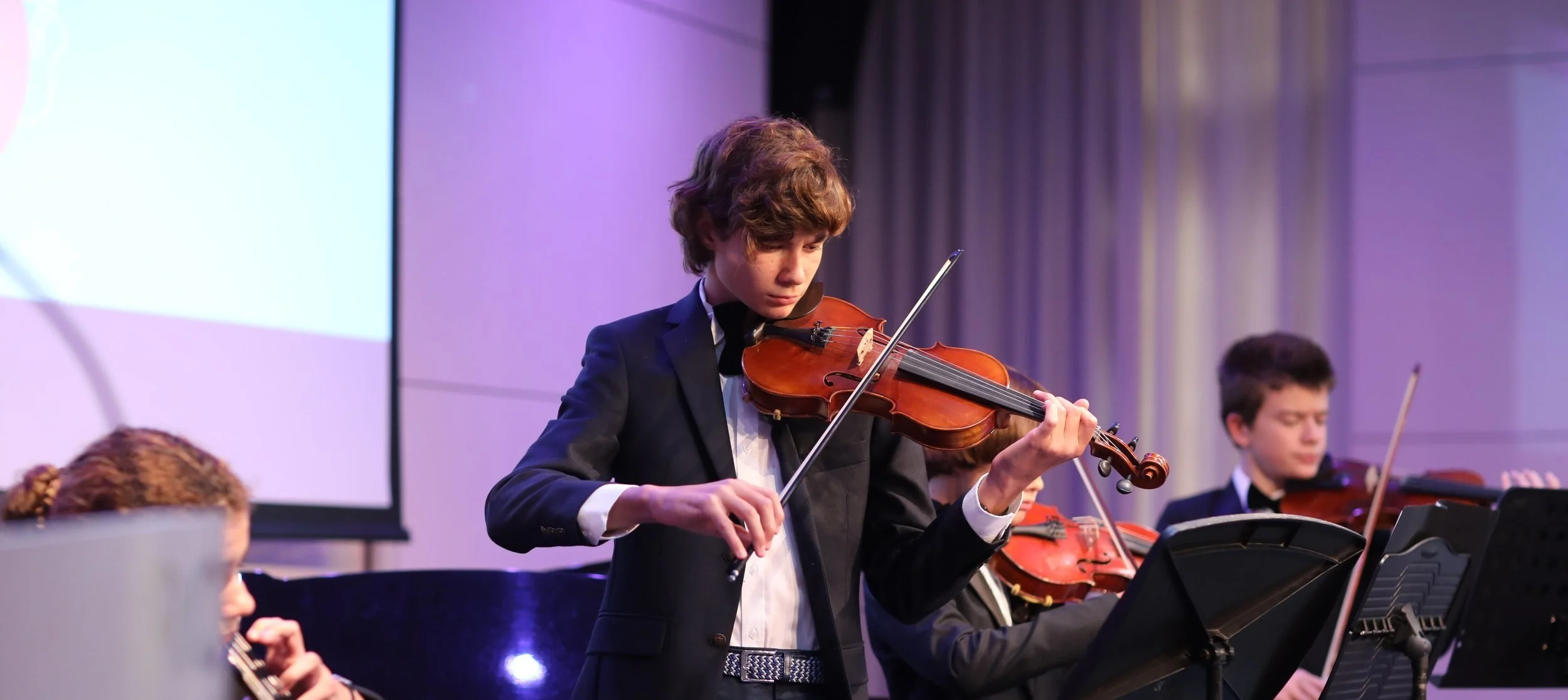 Young boy in a tuxedo playing the violin at a concert.