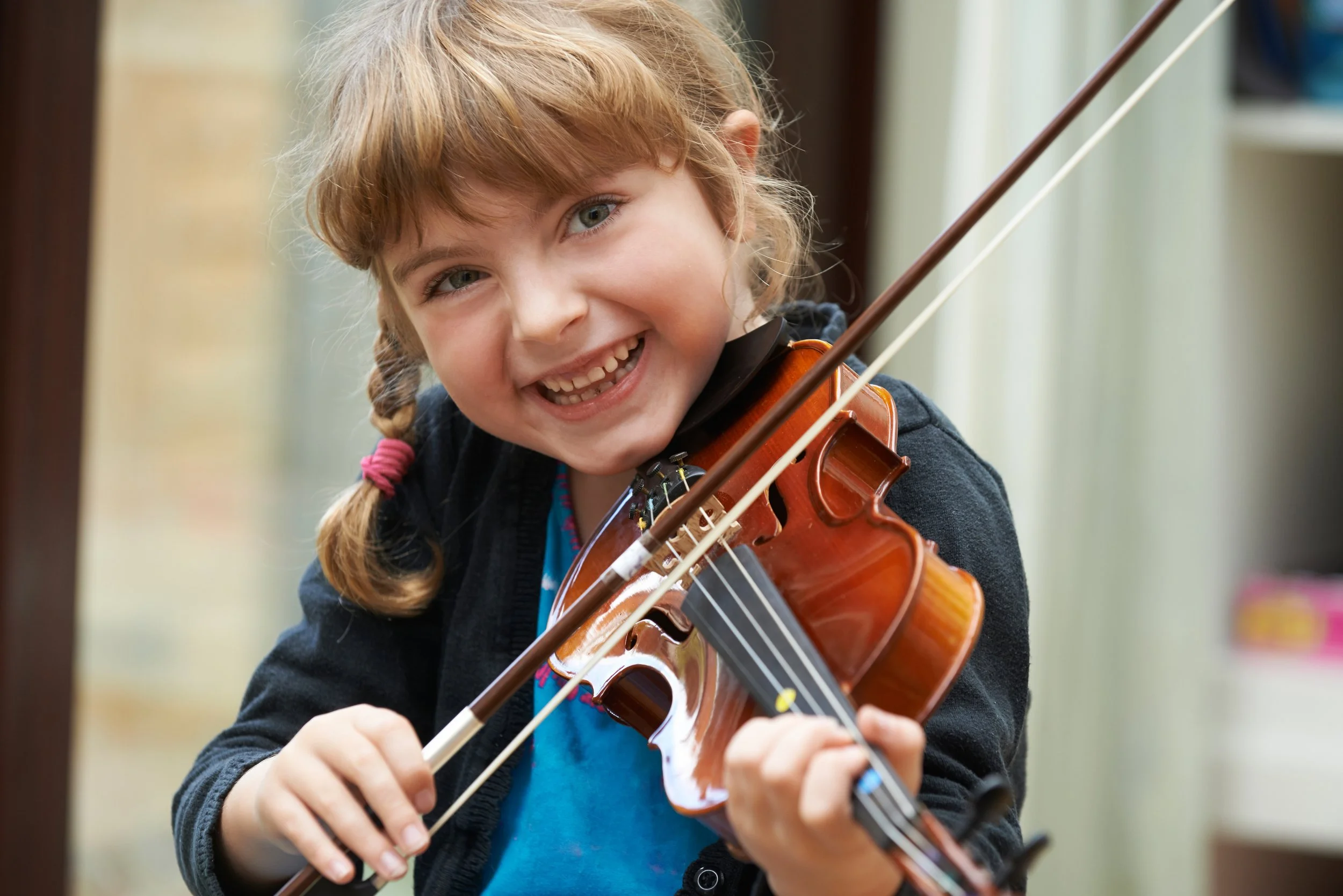 A young girl playing the violin and smiling at the camera.