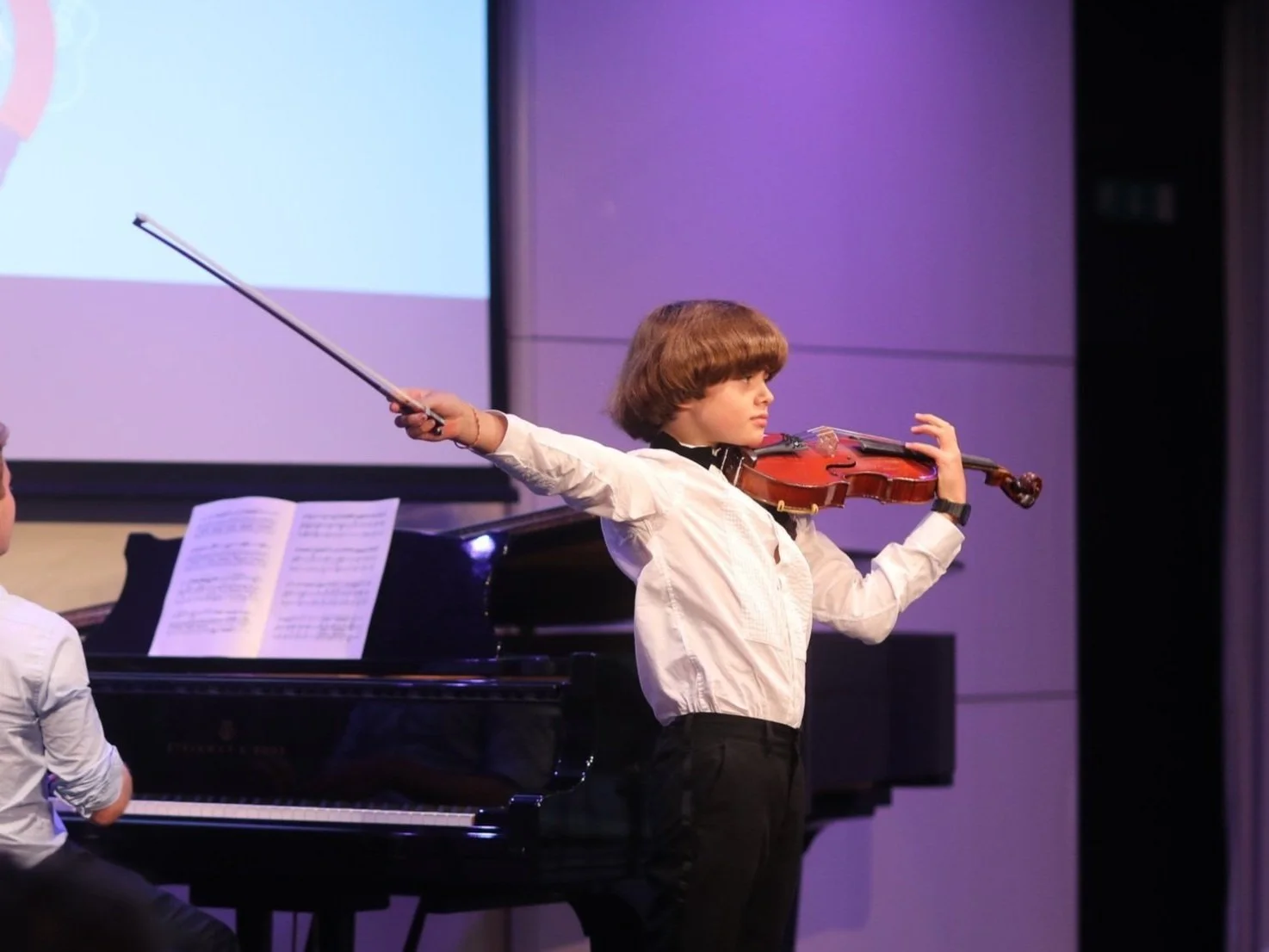 Boy at the end of violin recital with piano accompaniment.