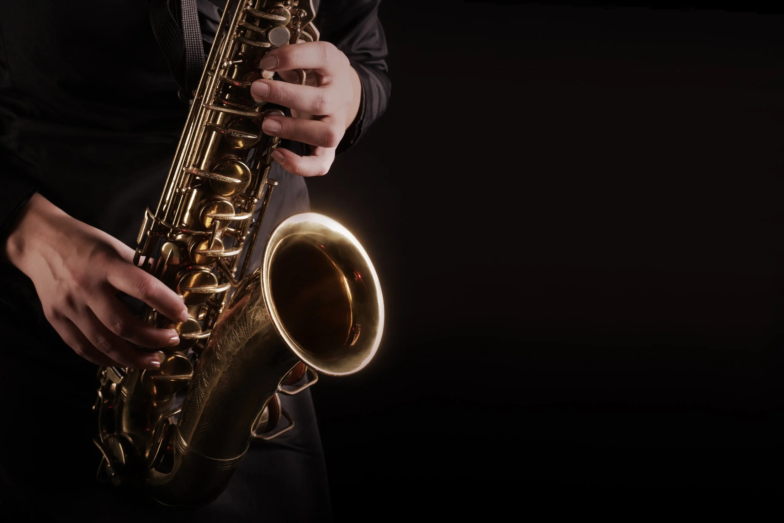 Close-up of hands playing the saxophone with shadowy background.