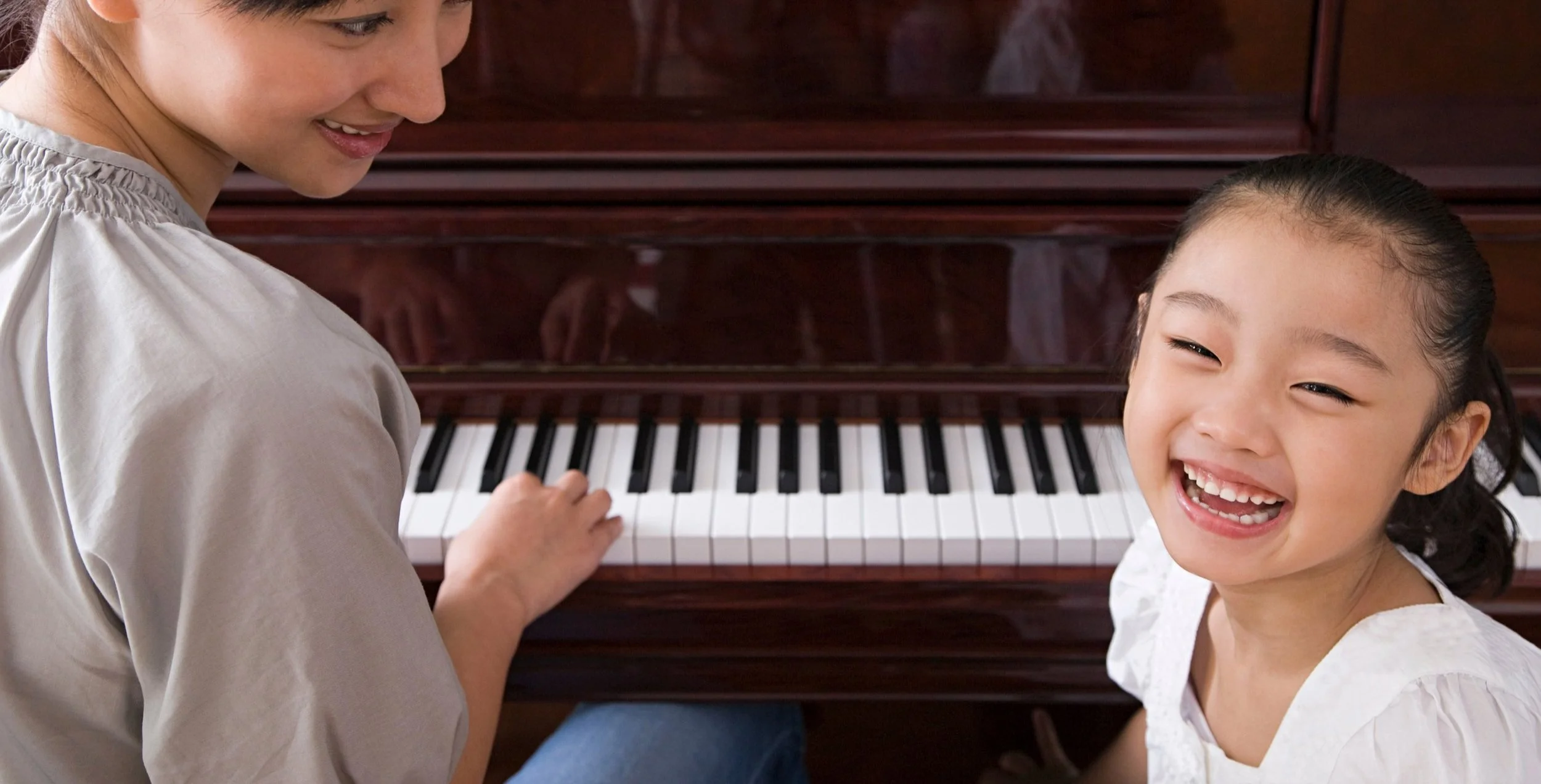 Young girl smiling during her piano lesson in London with teacher sat beside her.