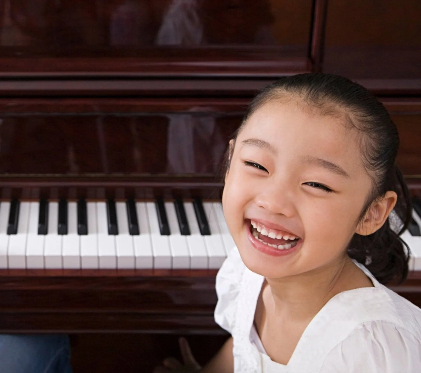 A young girl with a big smile sitting at a piano.