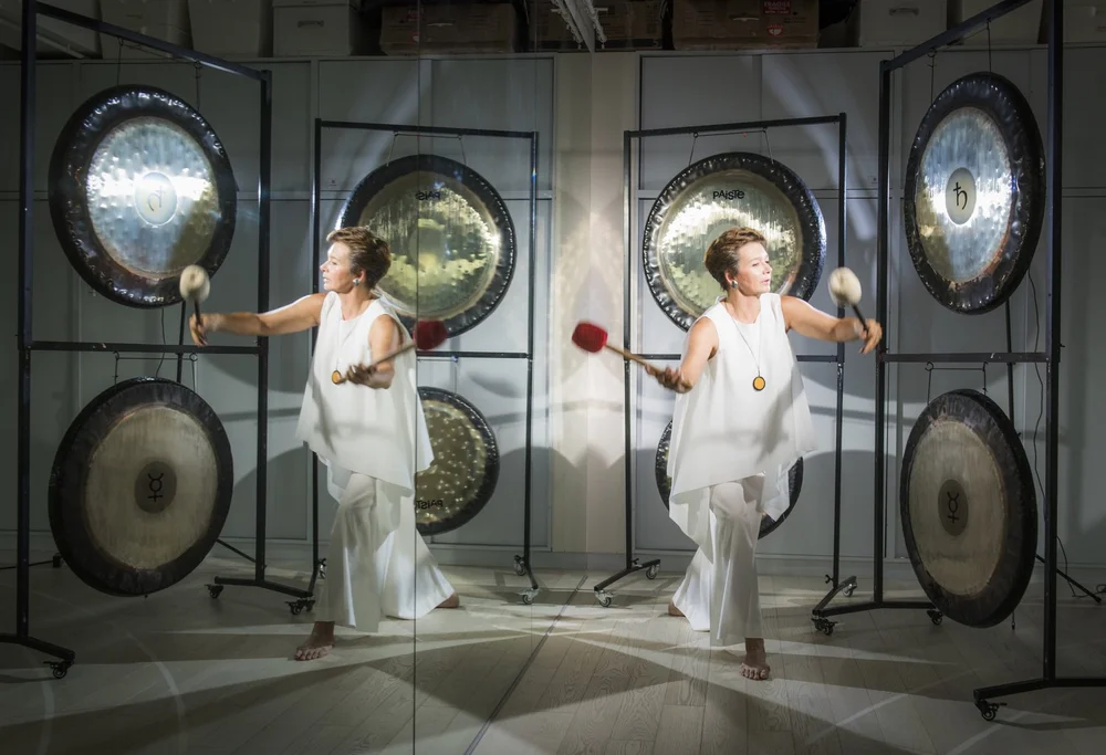 Martha Collard playing singing bowls in the Red Doors studio, gongs hanging behind her.