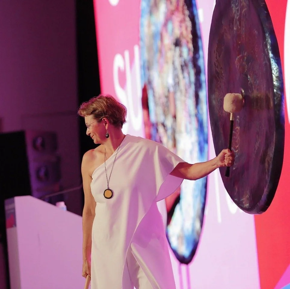 Martha Collard striking a gong on stage during a presentation