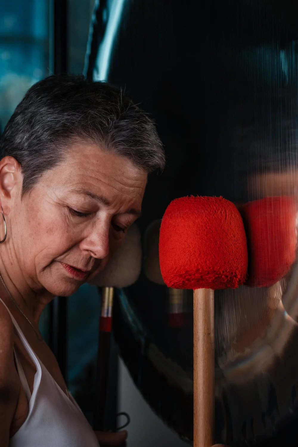 Martha Collard, eyes lowered, holding two red felt gong mallets in front of a large gong.