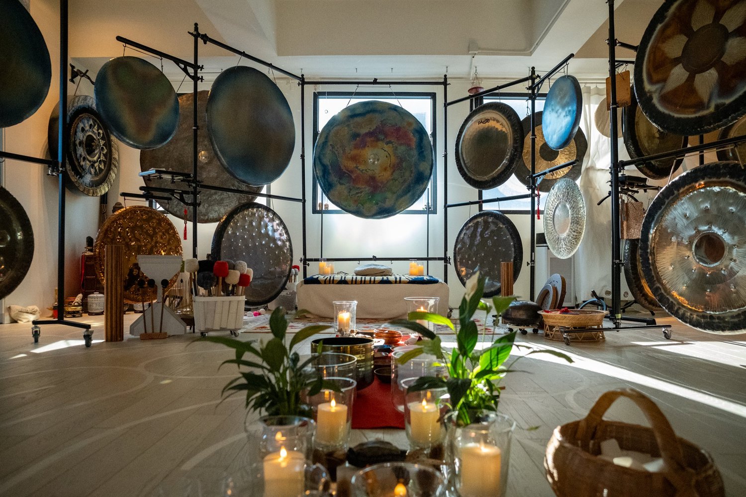 The Red Doors studio set for a gong bath: candles and plants on the floor, gongs of every size hanging on frames around the room.