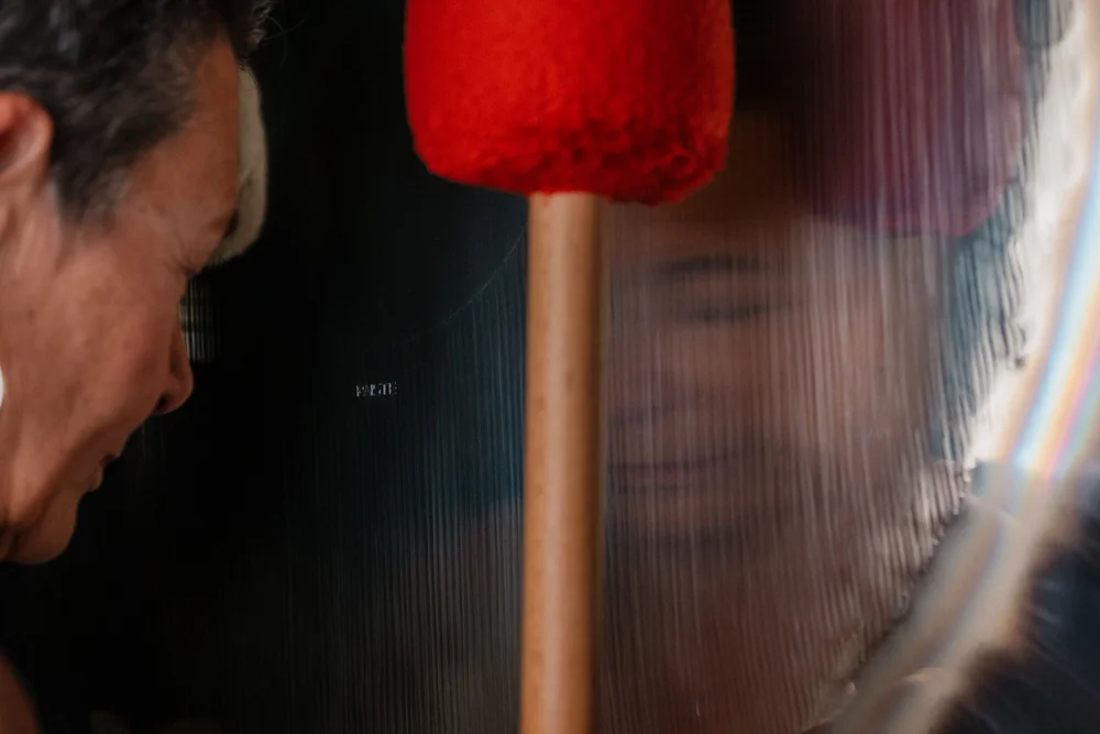 A red felt mallet against the shimmering face of a gong, Martha Collard leaning in to listen.