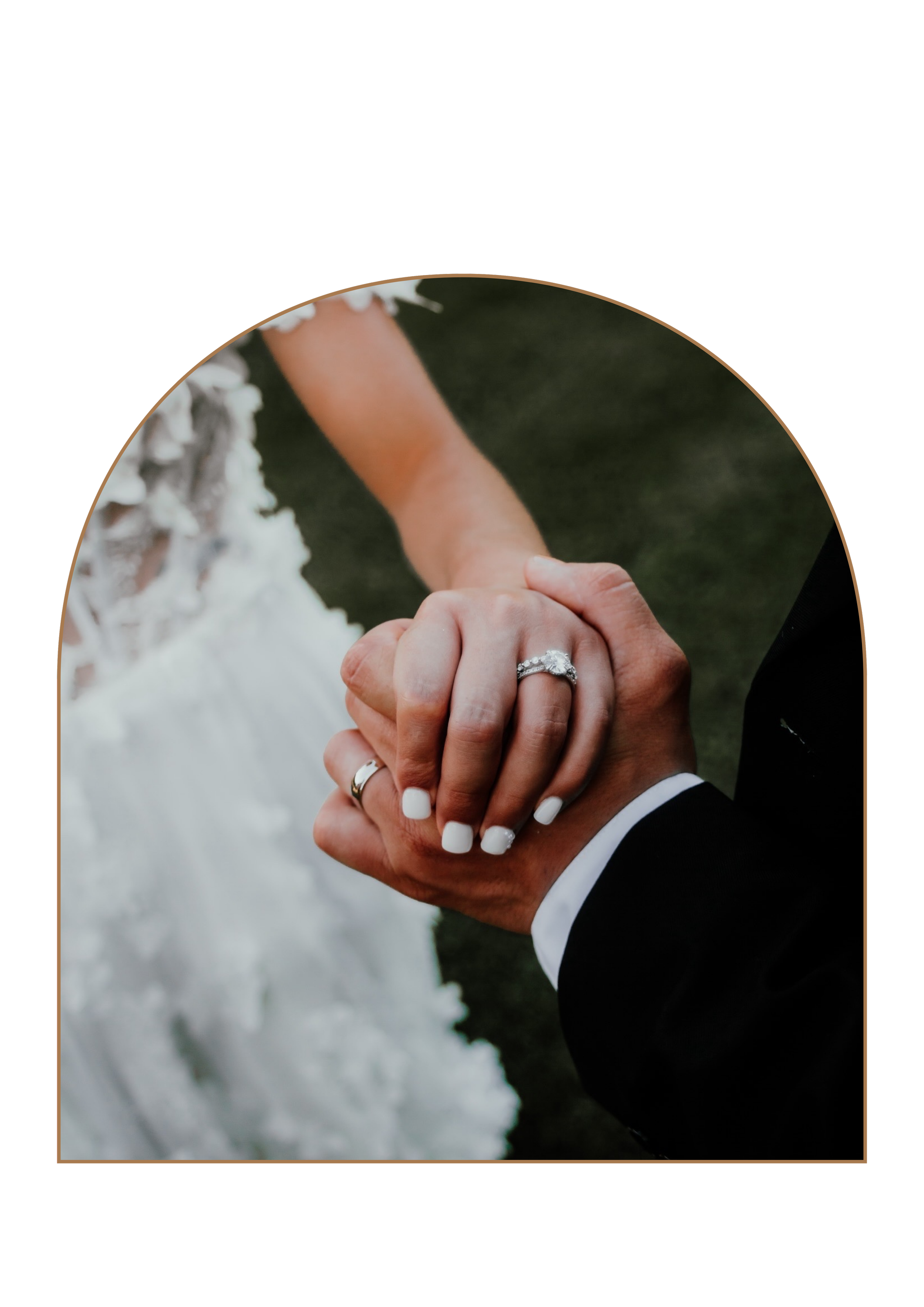 Close-up of a bride and groom holding hands, with wedding rings visible, outdoors with a green background.