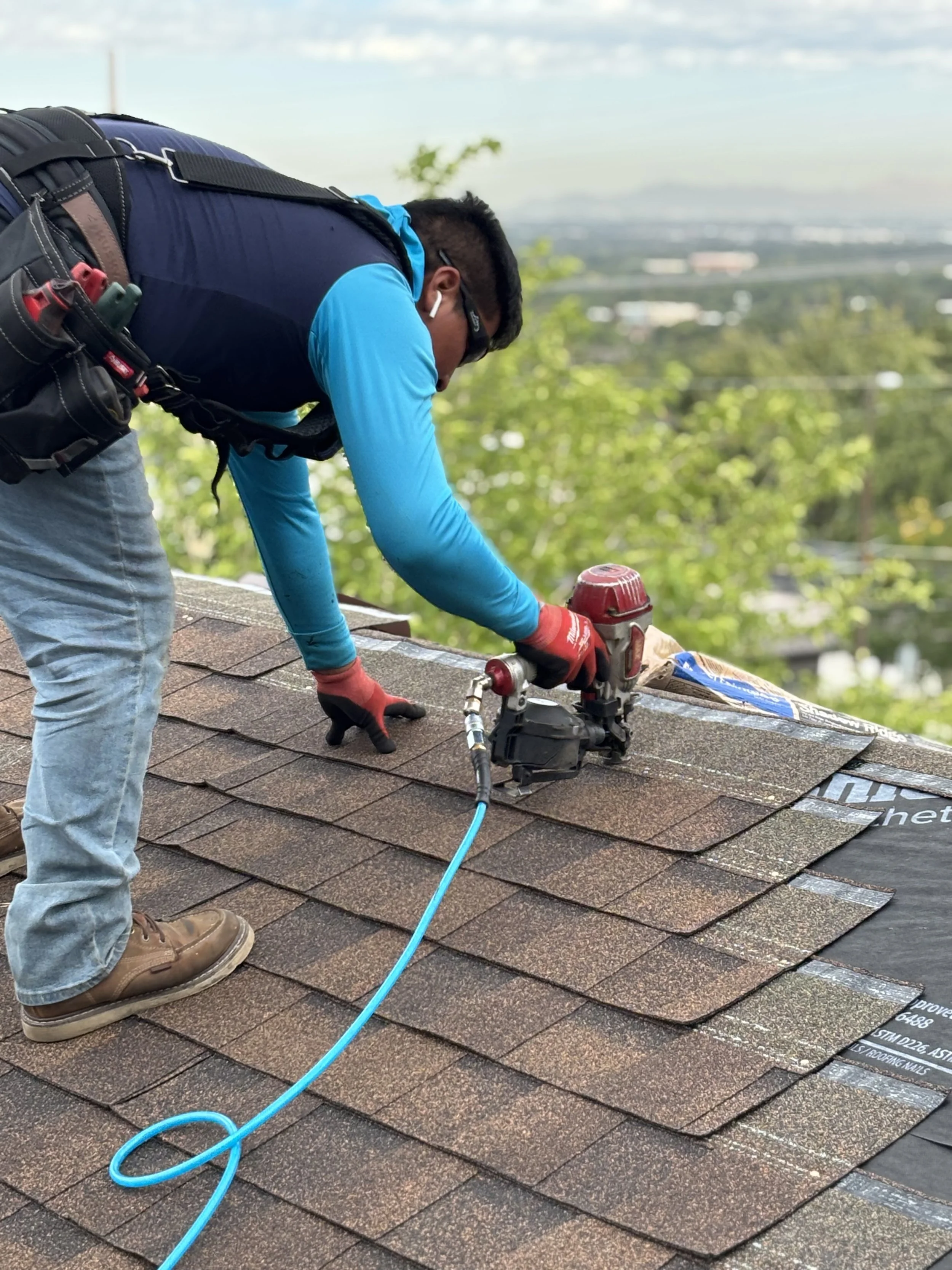 Man applying shingles to roof with mountains and city in the background