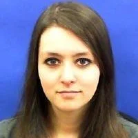 Portrait of a young woman with long dark hair, neutral expression, against a blue background.