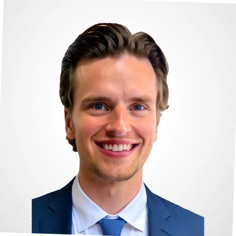 A young man in a blue suit with a white shirt and blue tie, smiling against a white background.