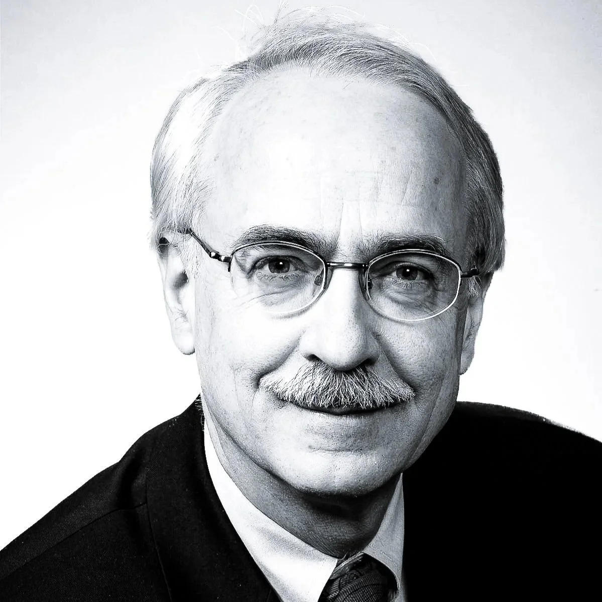 Black and white portrait of an elderly man with glasses, a mustache, and neatly combed hair, wearing a suit and tie.