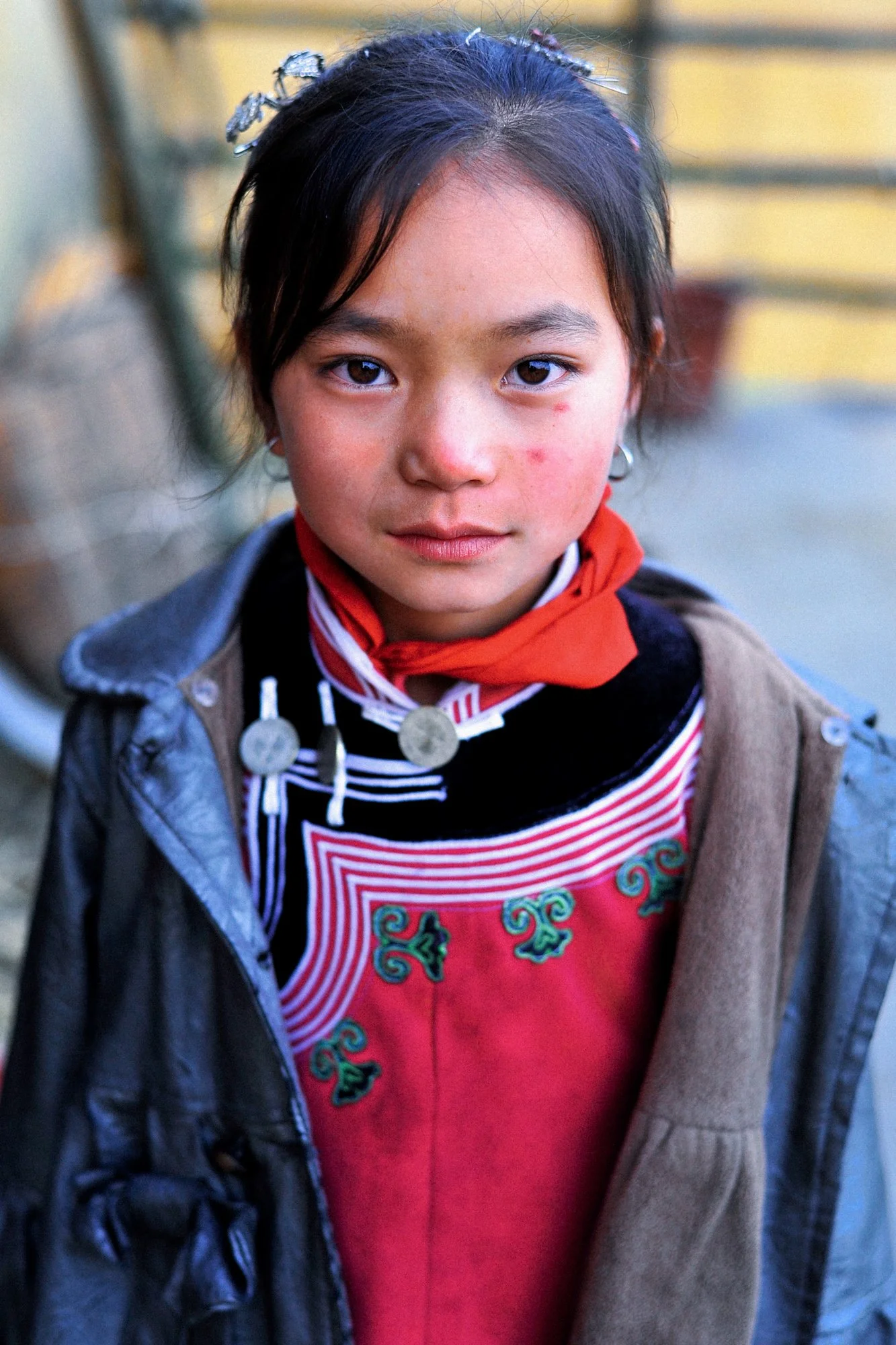 A young girl with dark hair, wearing traditional clothing and necklaces, looking directly at the camera.