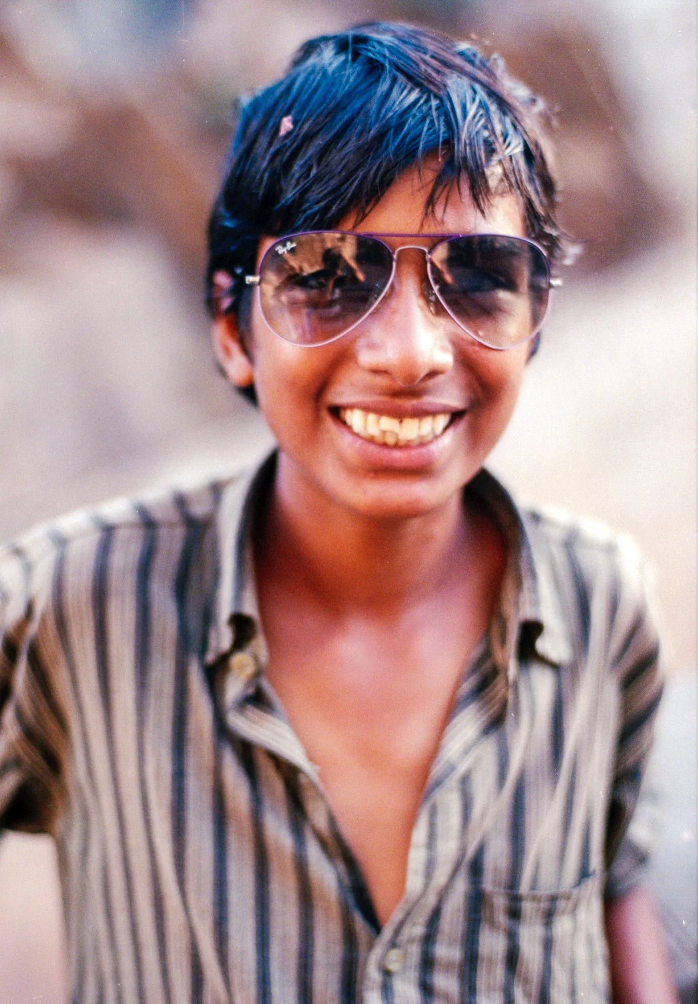 Smiling young boy wearing aviator sunglasses and a striped shirt.