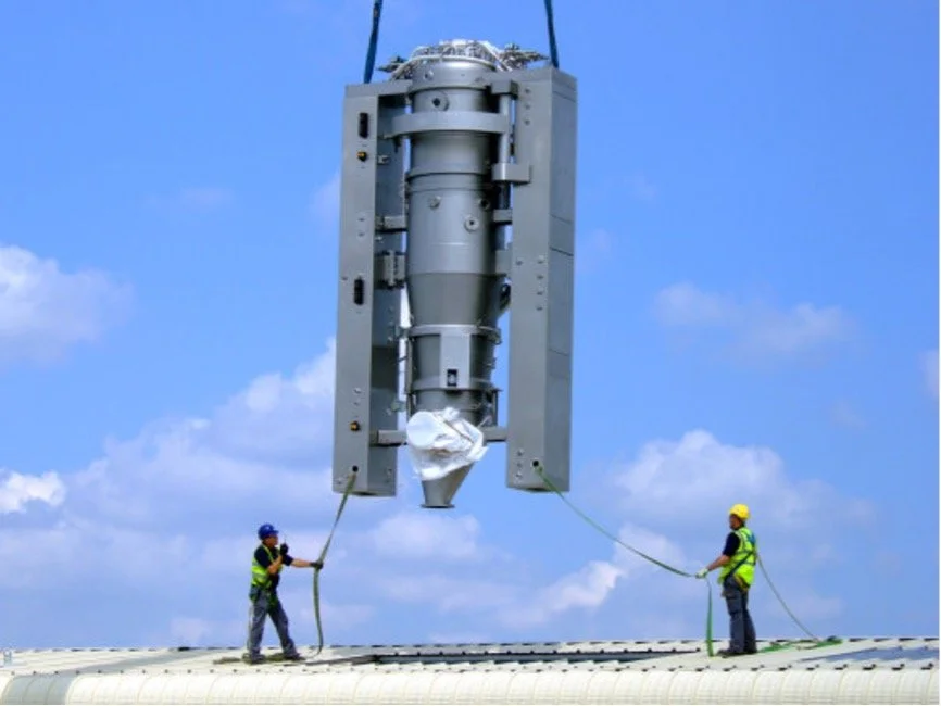 Two CIS employees are manoeuvring a large piece of machinery by ropes which is being held up by a crane