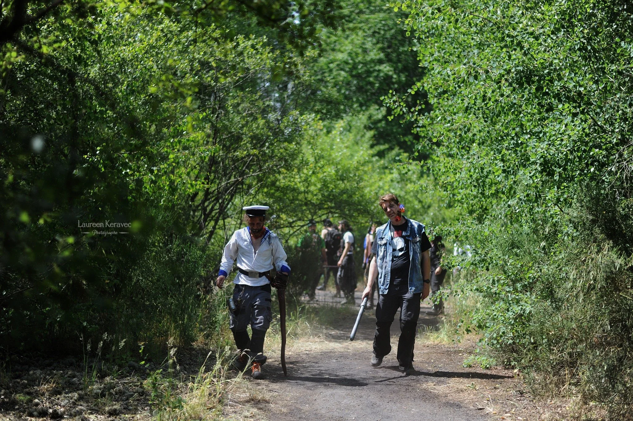 Groupe de personnes marchant dans une forêt verdoyante, certains utilisant des outils pour travailler le sol