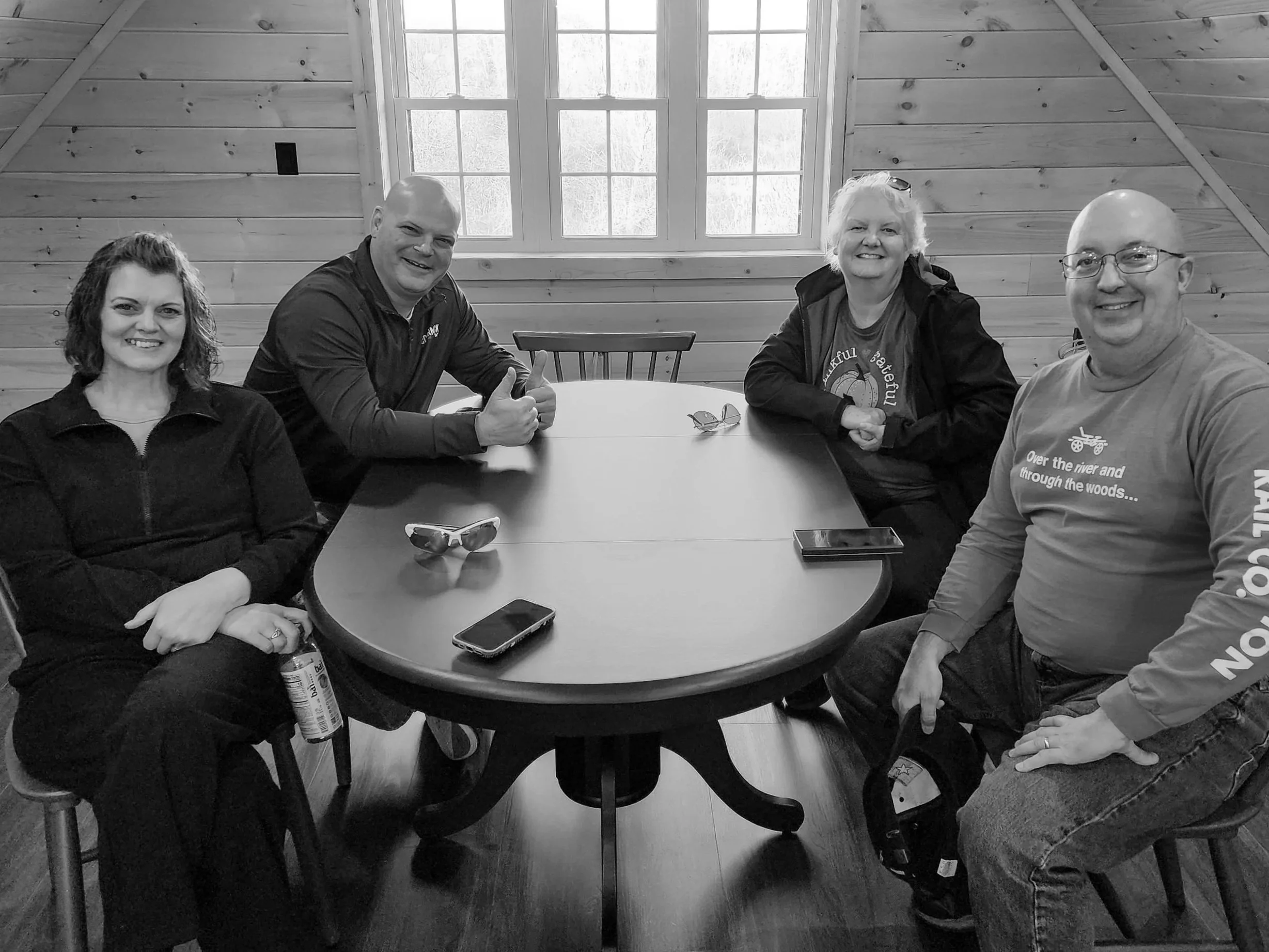 Four people sitting around a wooden table in a room with wooden walls and large windows, smiling and looking at the camera.