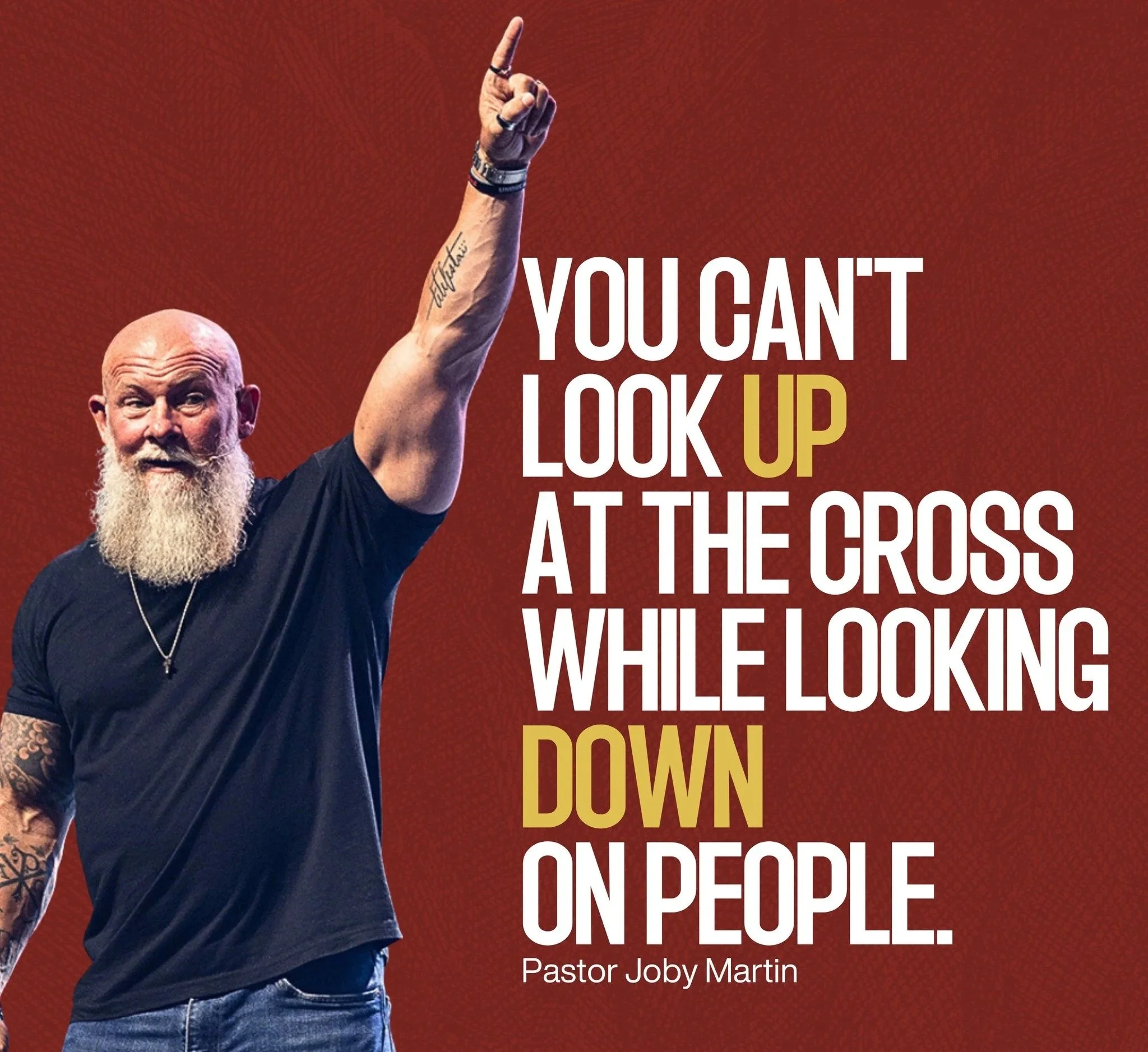 A man with a beard and tattoos wearing a black T-shirt, pointing upward with his right index finger, and a quote on the right side reading, "You can't look up at the cross while looking down on people," attributed to Pastor Joby Martin.