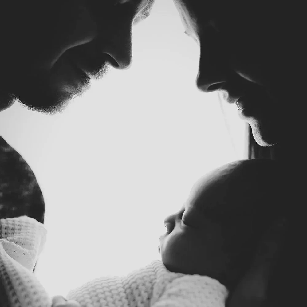 Une famille regarde tendrement un bébé, en noir et blanc.