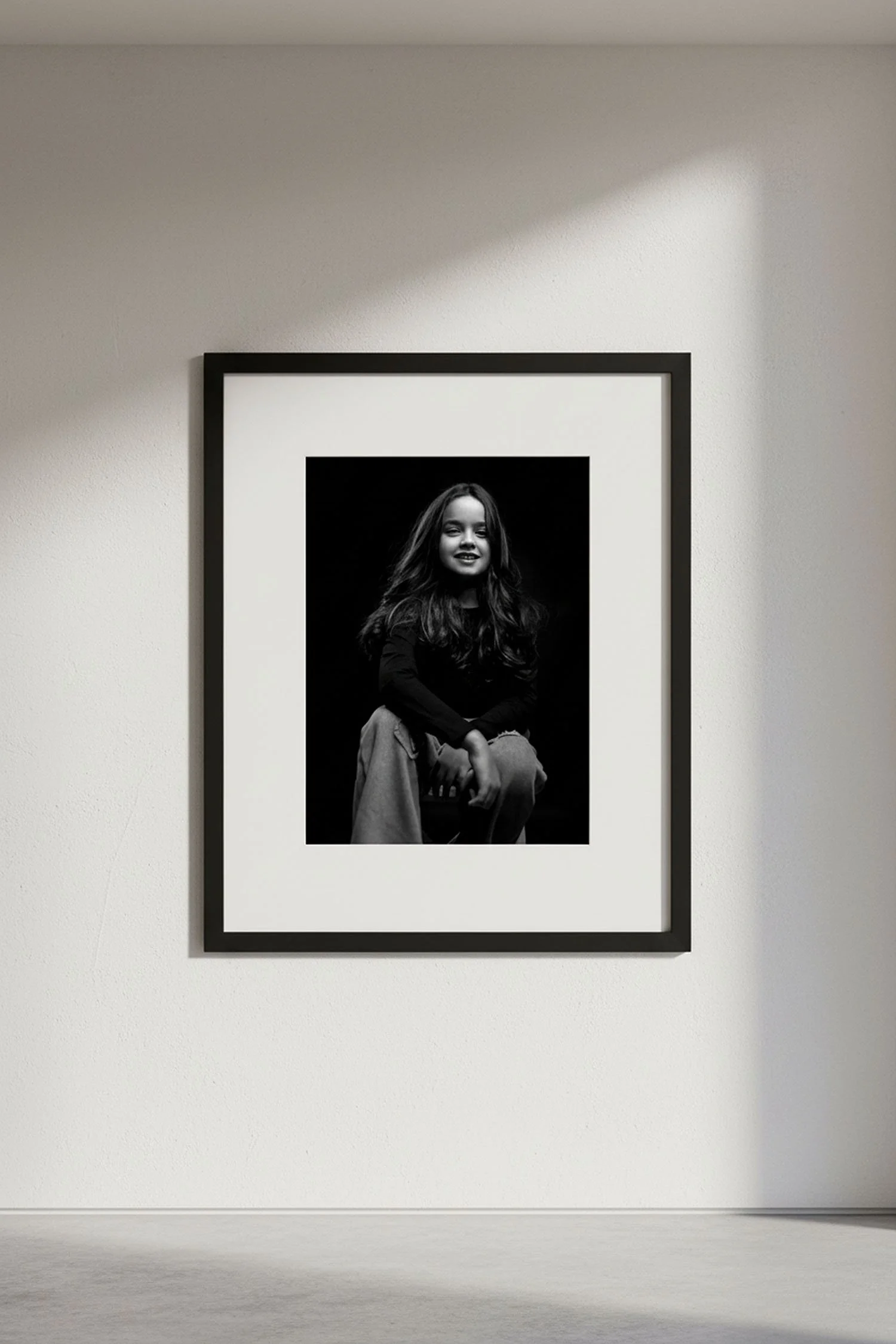 Photographie en noir et blanc d'une jeune fille souriante, assise, exposée dans un cadre encadré sur un mur blanc d'une galerie d'art.