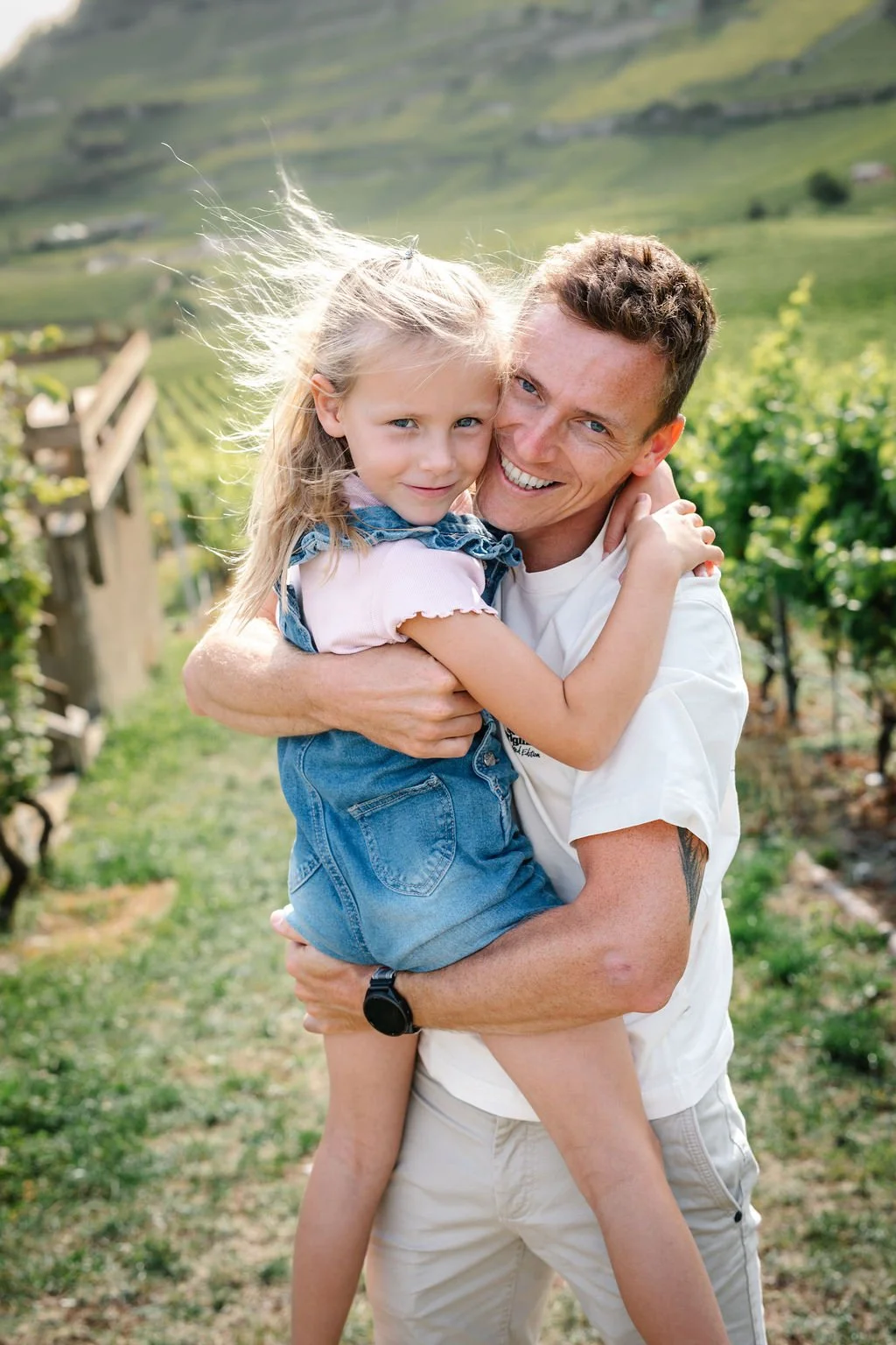 Un homme et une jeune fille, tous deux souriants, en train de s'embrasser dans un vignoble en plein air.