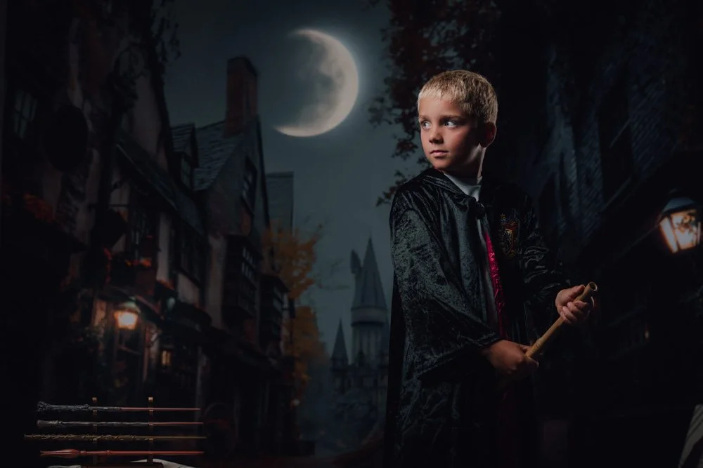 Un jeune garçon habillé en vampire avec une cape noire tient un bâton dans une rue sombre, sous une pleine lune, avec un château en arrière-plan.
