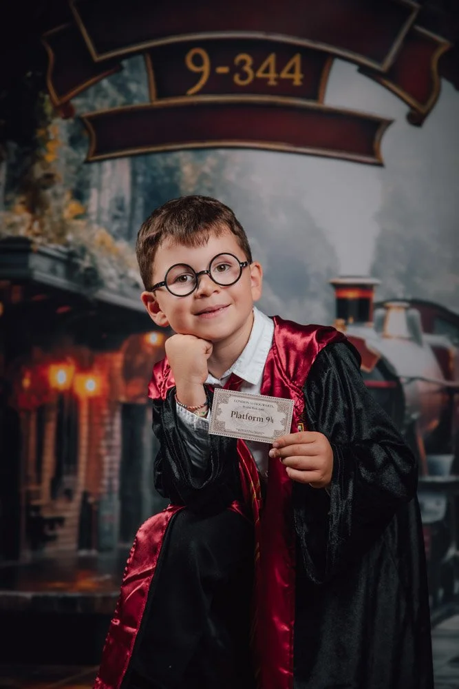Enfant déguisé en Harry Potter, portant des lunettes rondes et une robe de sorcier, tenant un billet pour la plateforme 9¾, posant devant un décor de train et d'éléments magiques.