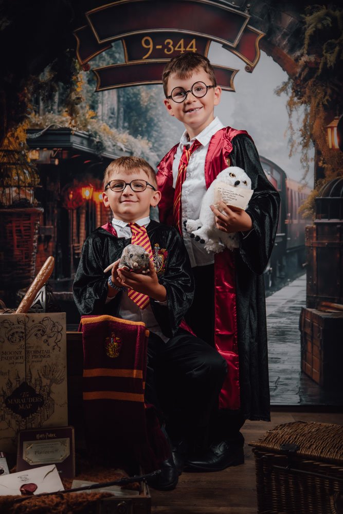 Deux enfants habillés comme des personnages de Harry Potter posent avec des objets magiques dans une scène d'école de sorcellerie, avec un décor de quai de gare.