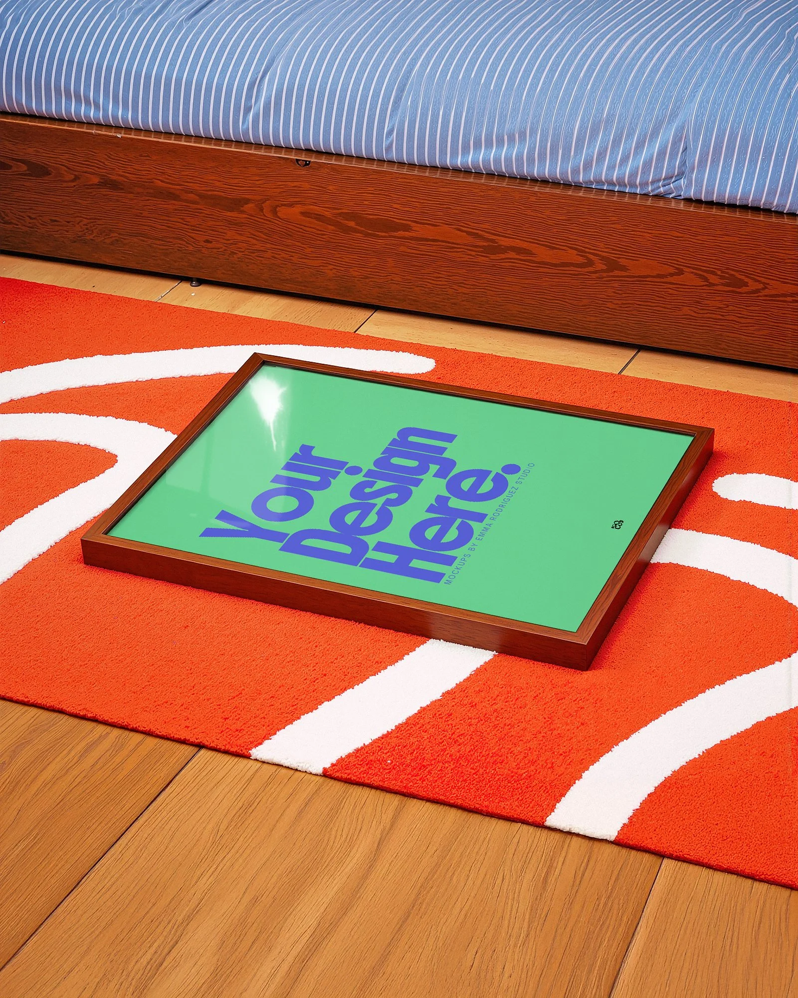 Framed sign on a colorful rug with orange, white, and red pattern, placed on a wooden floor, with a bed with a wooden frame and blue striped bedding in the background.
