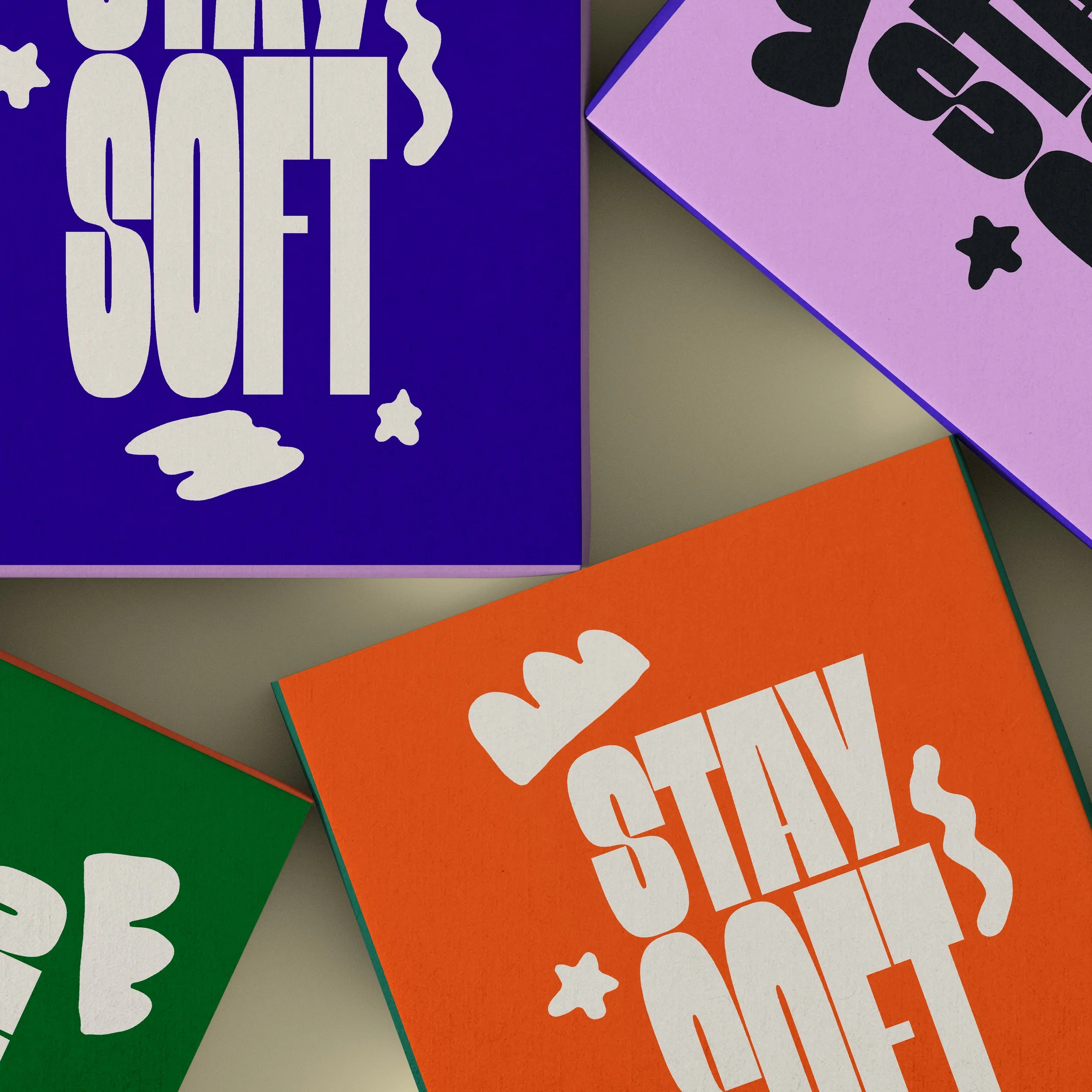 Colorful boxes with playful typography reading 'STAY SOFT,' 'STAY GOLD,' and 'LOVE' in bold letters with hearts and stars, arranged on a light-colored surface.