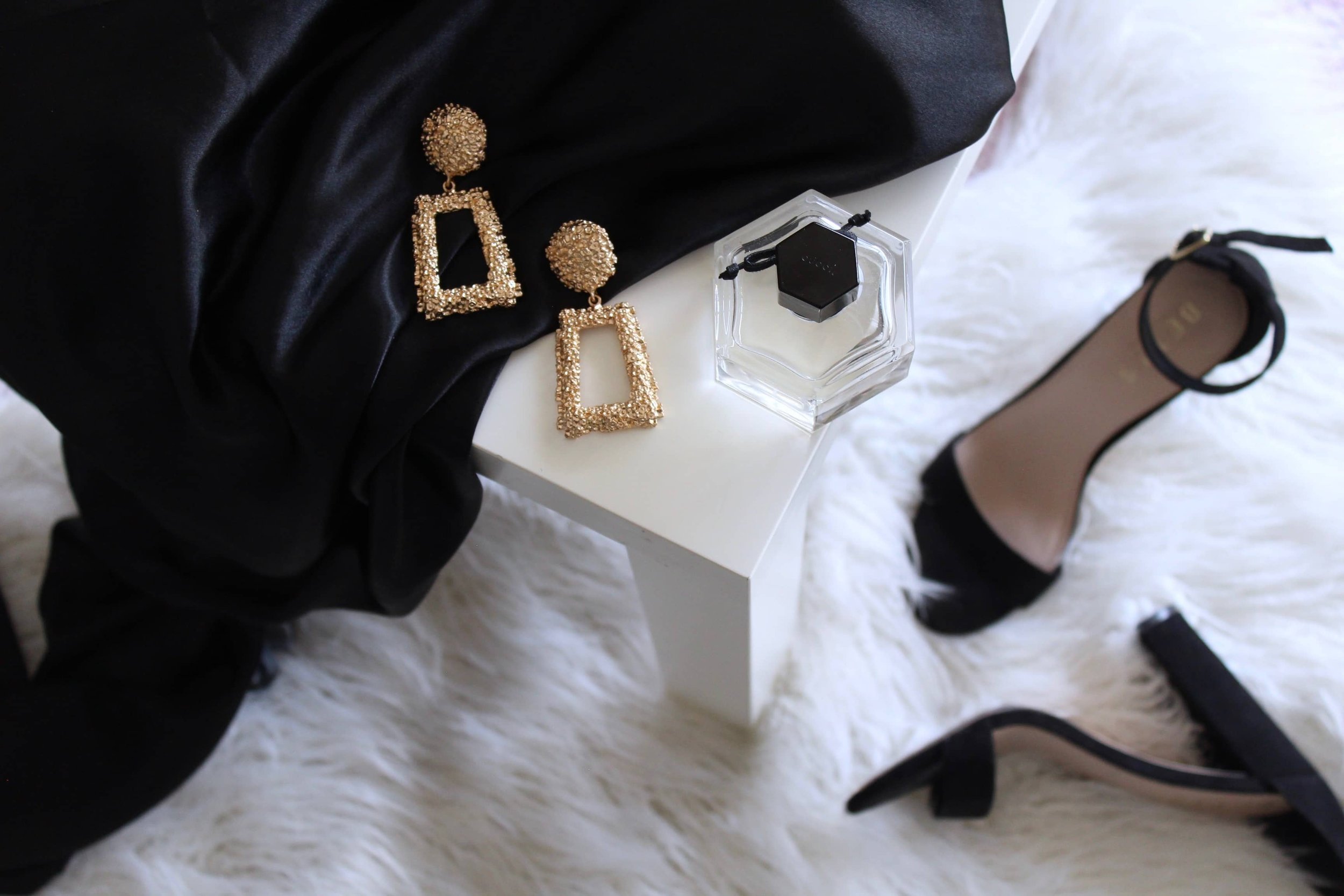 Flat lay of black heels, gold earrings, and perfume symbolising luxury e-commerce and optimised customer journeys
