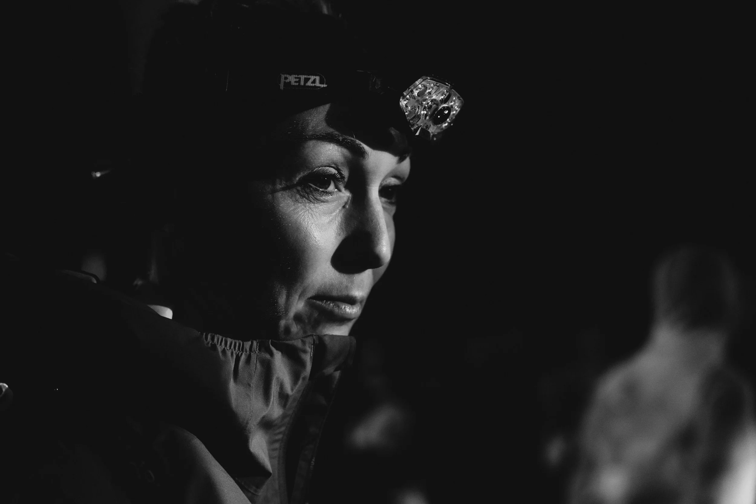 Frau mit Stirnlampe in dunkler Umgebung, trägt eine Jacke