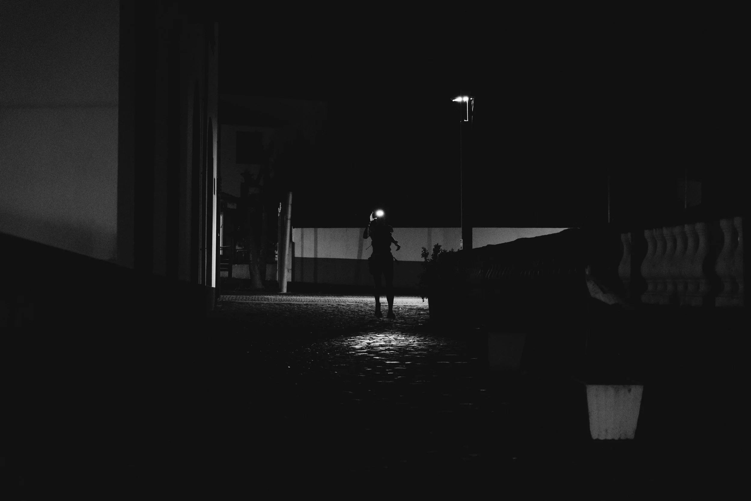 Eine Person mit einem Helm, die nachts in einer dunklen Umgebung steht, beleuchtet von einer Taschenlampe.