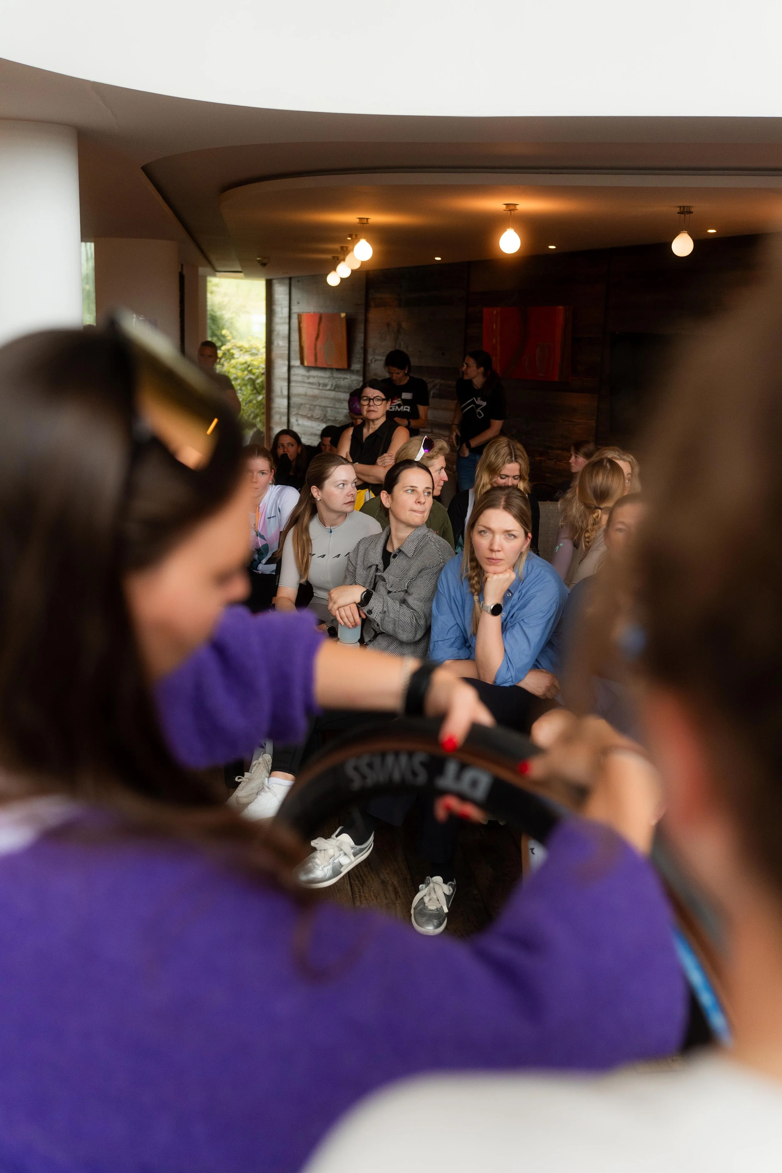 Eine Gruppe von Frauen sitzt in einem Raum, während eine andere Person im Vordergrund eine Kamera hält und filmt.