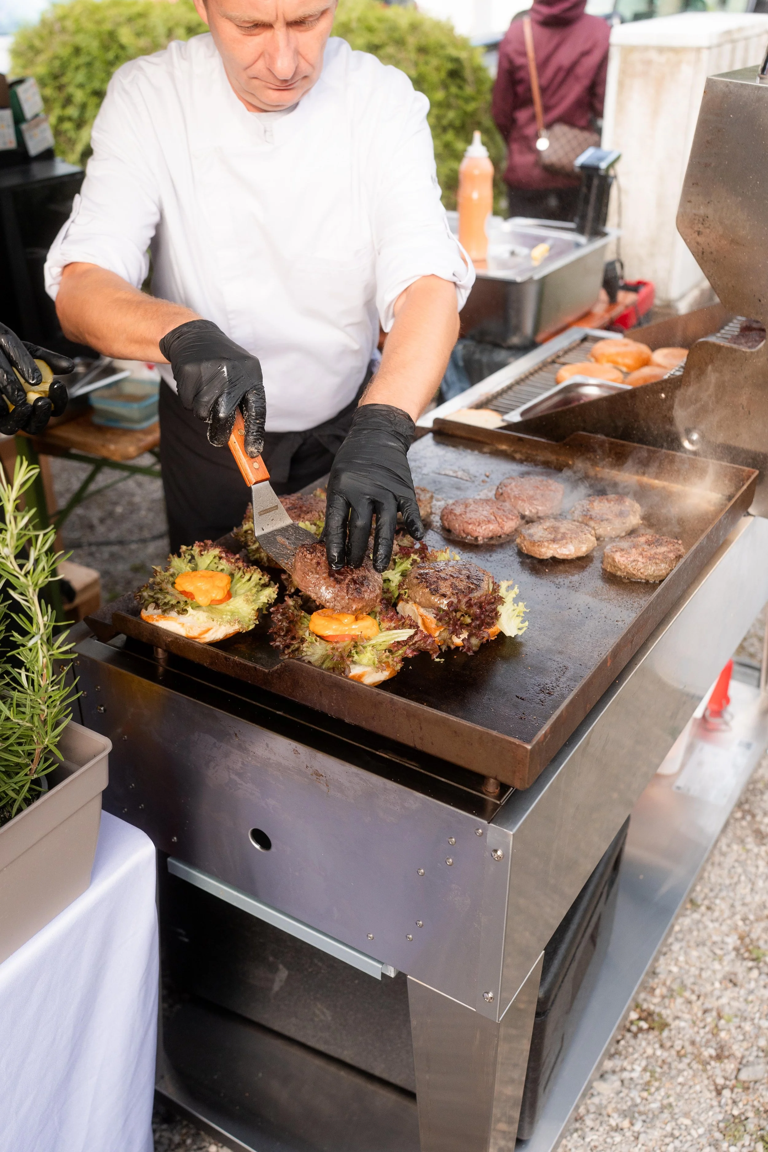 Ein Koch bereitet Hamburger Patties auf einem Grill vor, während er sie auf Salatblätter legt, die auf dem Grill liegen.