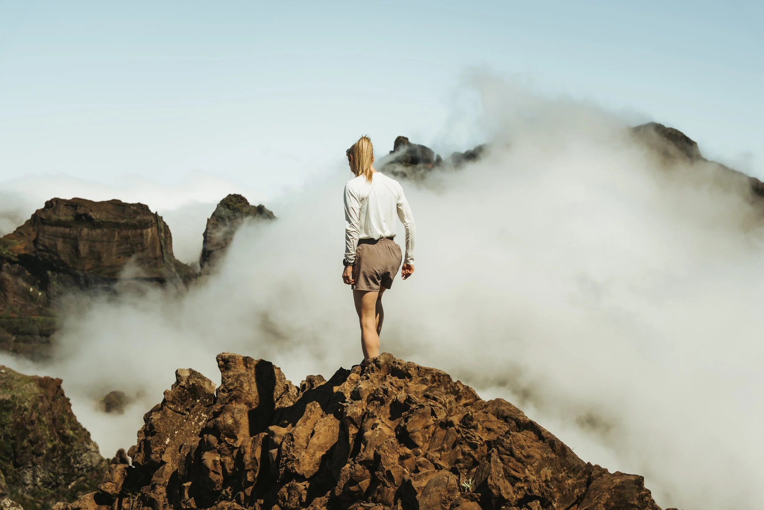 Eine Frau steht auf einem Felsen und schaut auf eine neblige Berglandschaft.