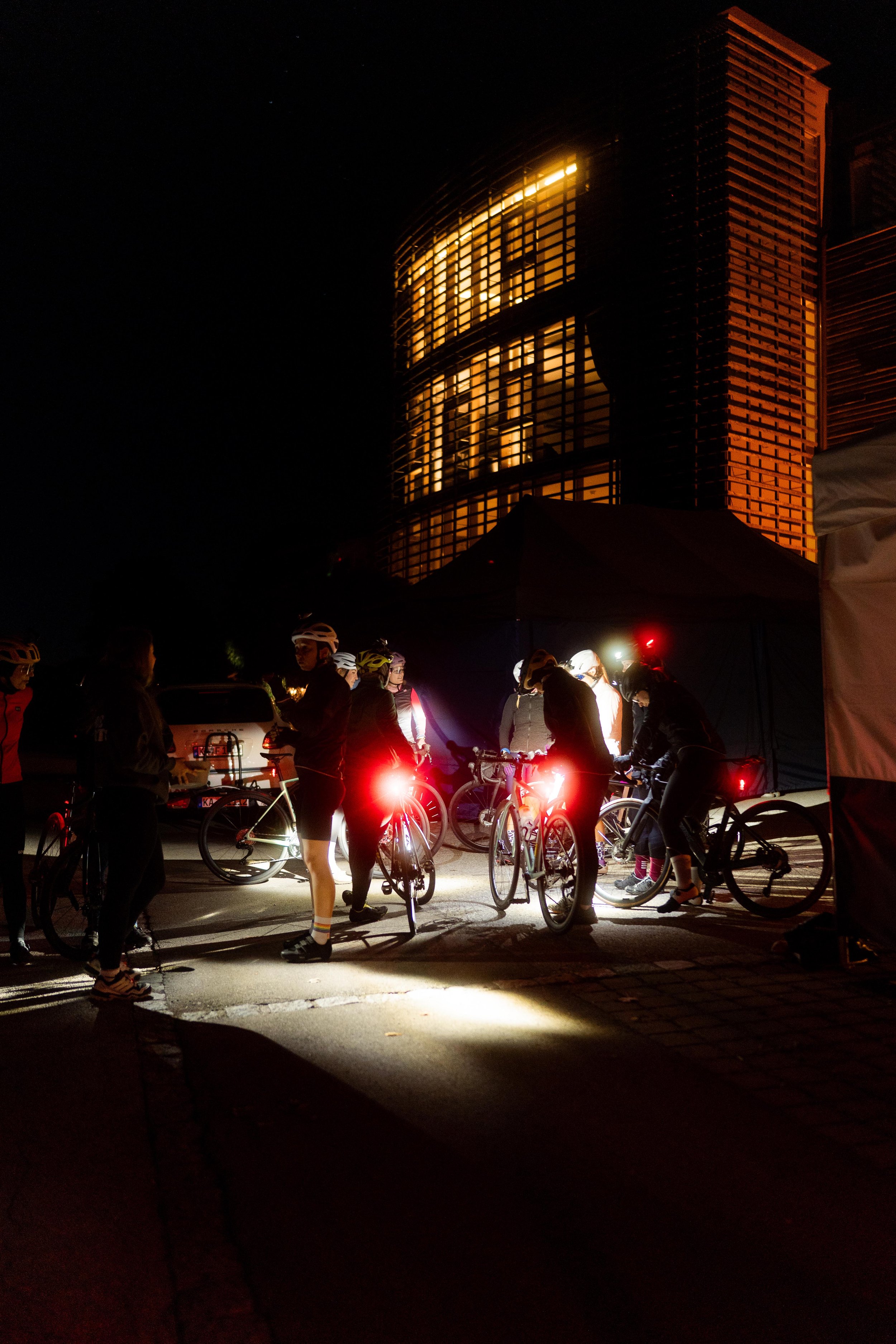 Menschen versammelt sich bei Fahrradnachtveranstaltung nächtlich, im Hintergrund ein modernes Hochhaus, leuchtende Fahrradlichter sichtbar.