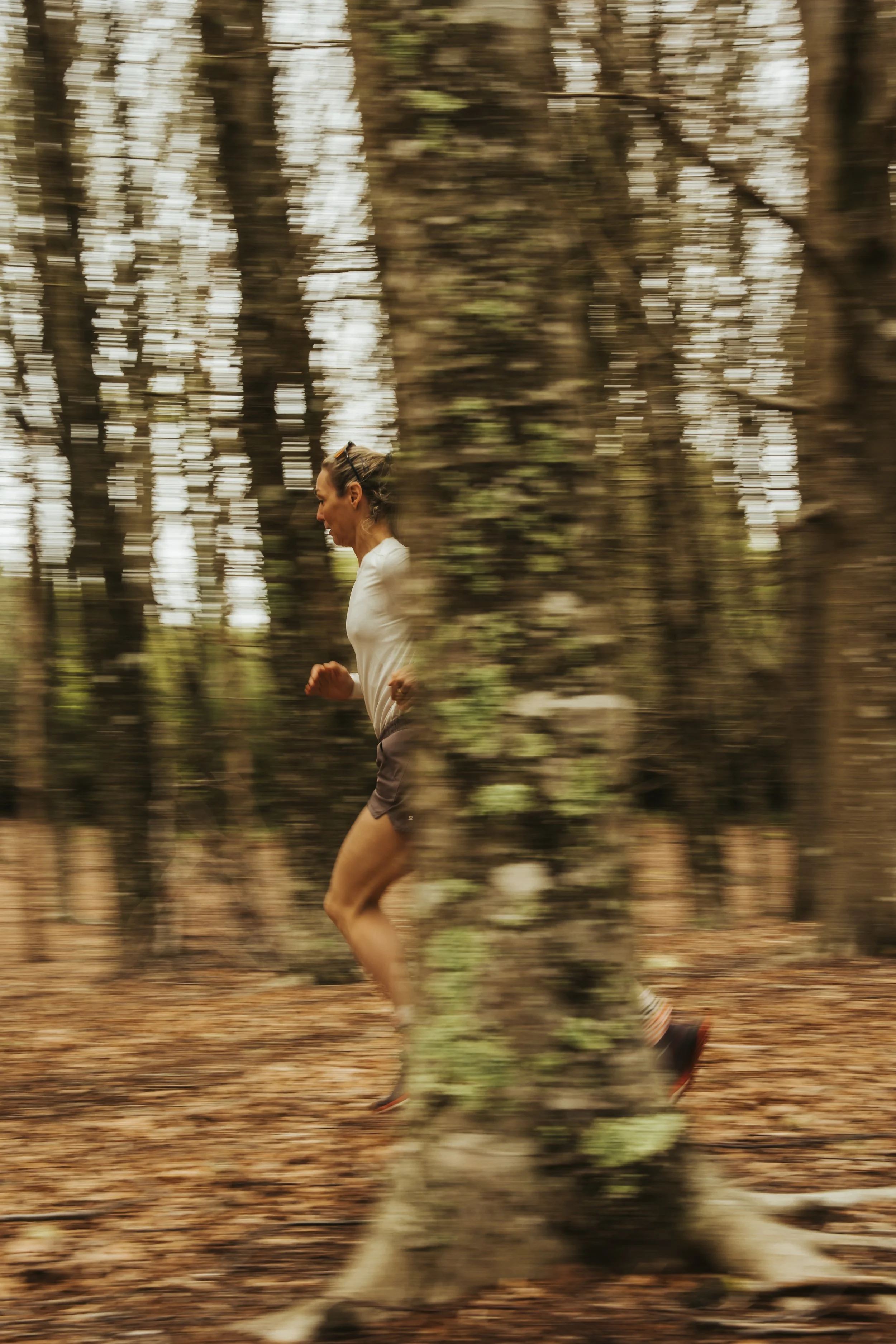 Frau läuft durch einen Wald, unscharf im Hintergrund, Bewegung erkennbar.