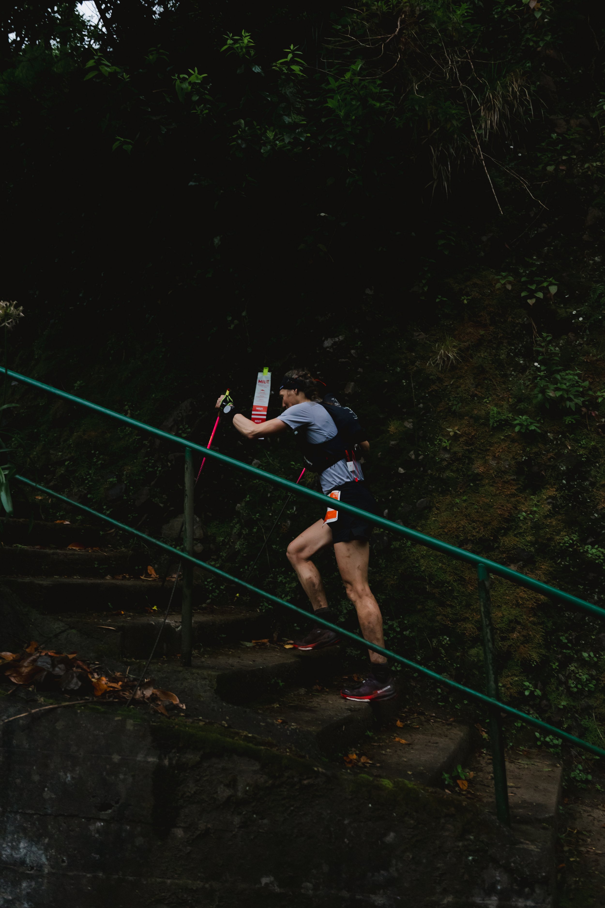 Frau beim Bergsteigen im Wald, trägt Laufkleidung und Rucksack, erklimmt Stein Treppe mit Geländer.