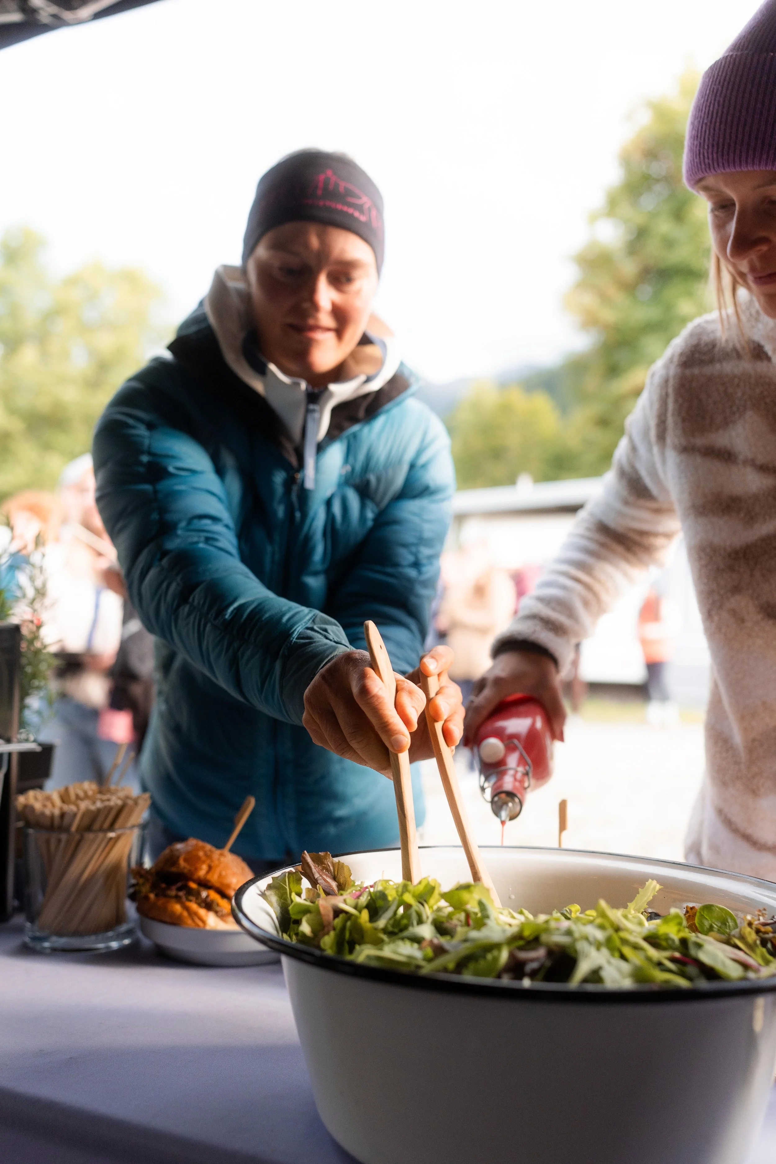 Menschen servieren einen Salat bei einem Outdoor-Buffet.